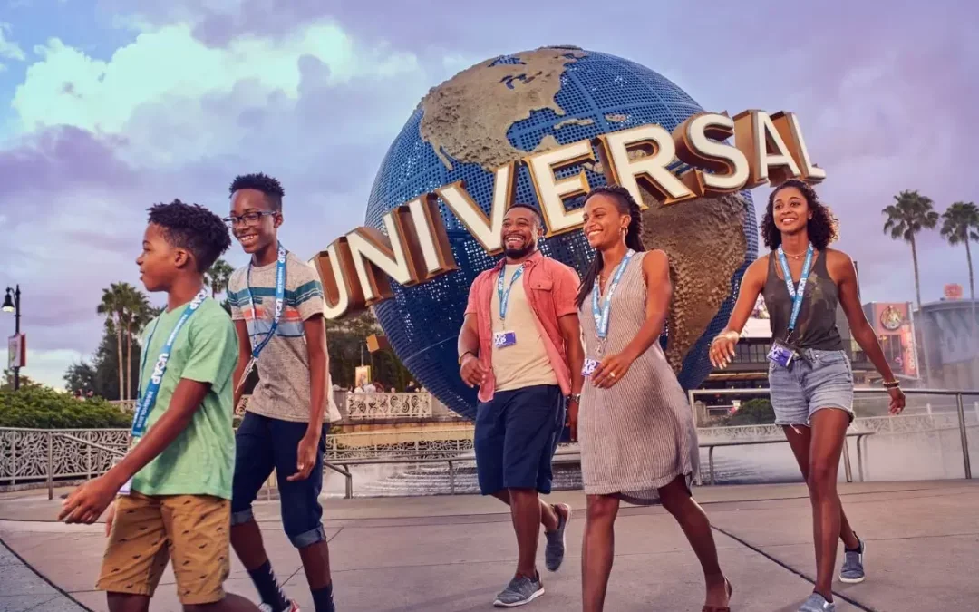 A diverse group of five people walking in front of the Universal Studios globe at an amusement park.