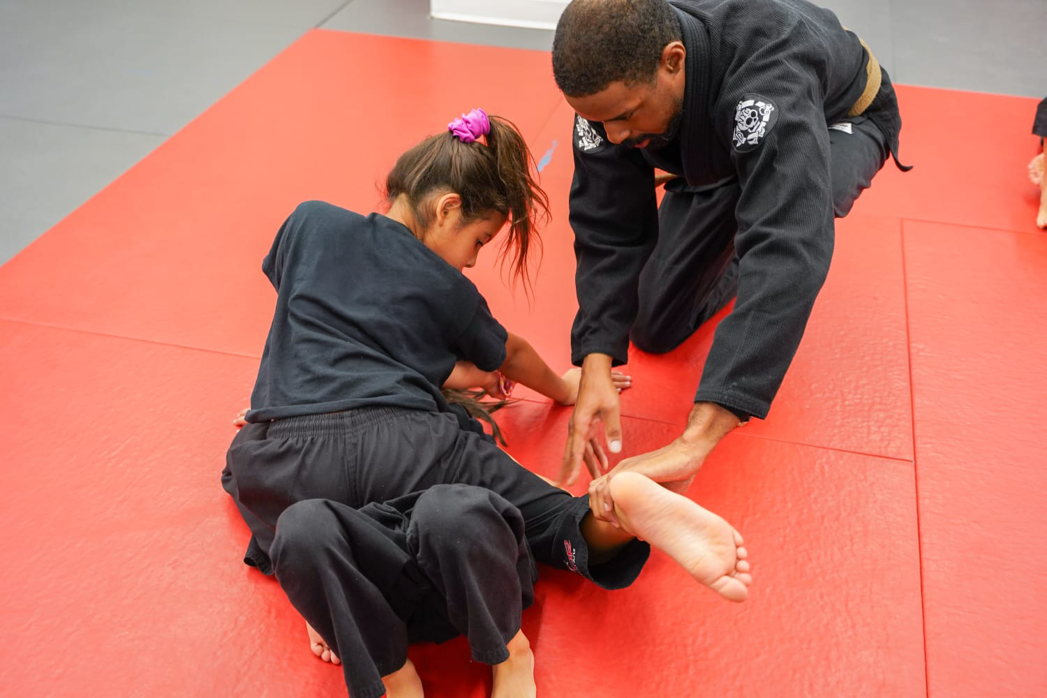 Instructor teaching a child Brazilian Jiu-Jitsu on a red mat.