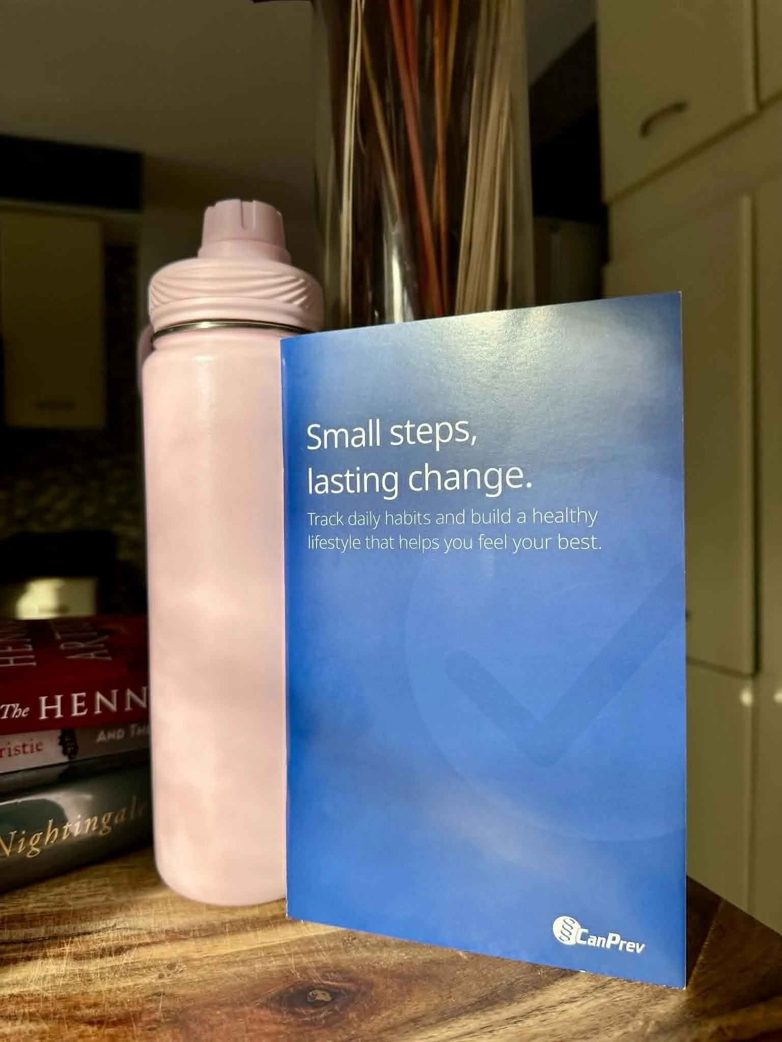 A booklet on top of a wooden cutting board next to a pink water bottle