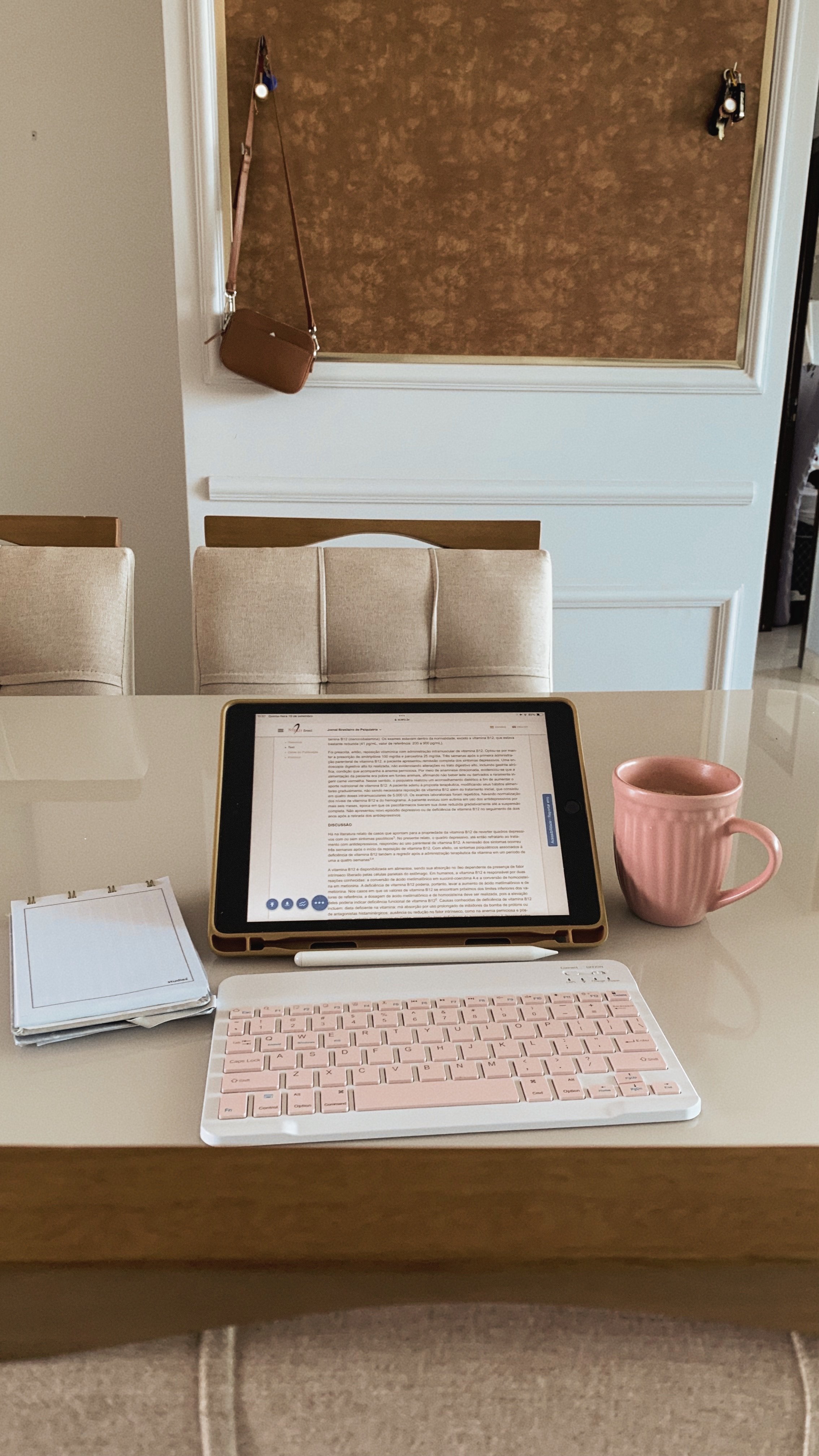 An ipad with pink keyboard, pink mug and notebook.