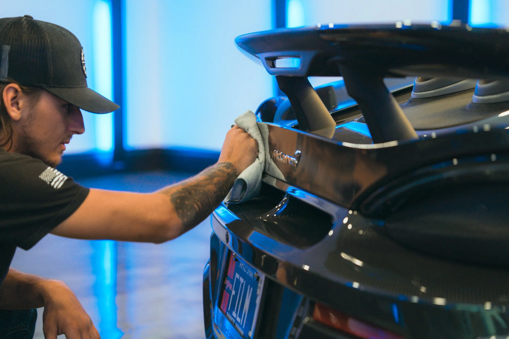 A man wearing a cap and black shirt is cleaning or polishing the front of a black vehicle with a cloth.