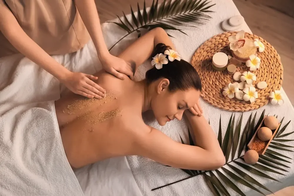 Woman receiving a back massage at a spa with flowers, candles, and spa products around her.