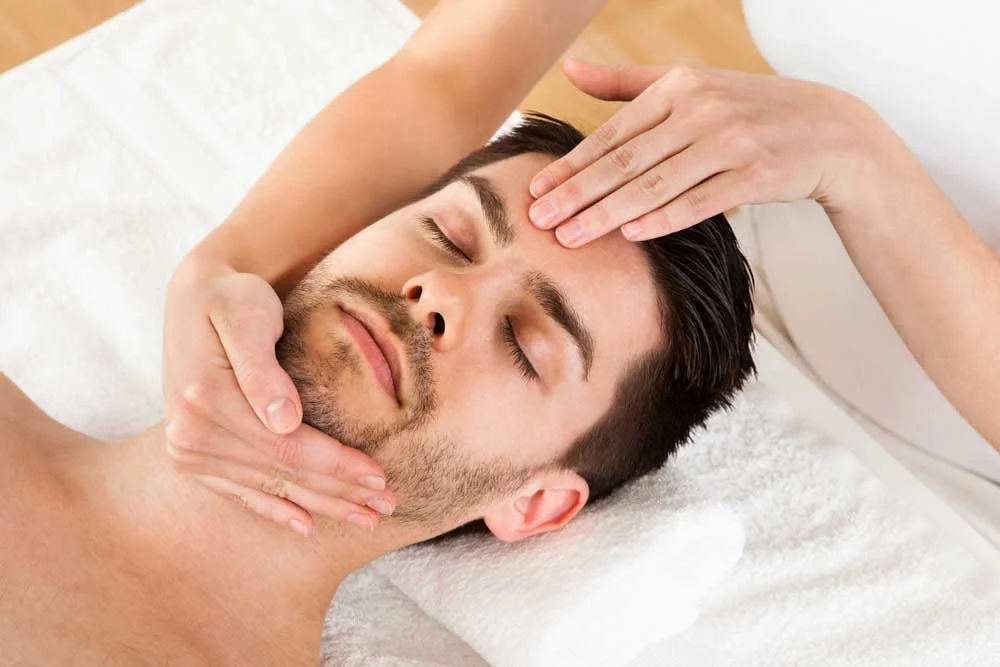A man receiving a facial massage at a spa or therapy session.