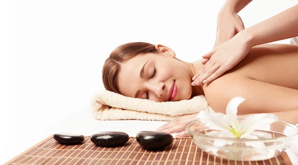 Woman receiving a back massage at a spa, lying face down with a towel under her head, with massage stones and a flower nearby.