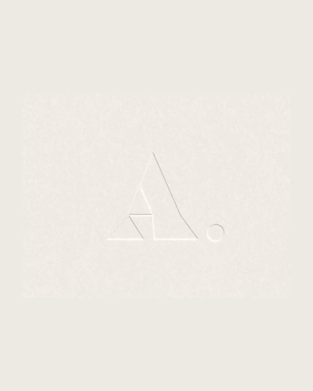 Minimalist embossed logo with a stylized letter 'A' and a small circle on the right, on a white textured background.