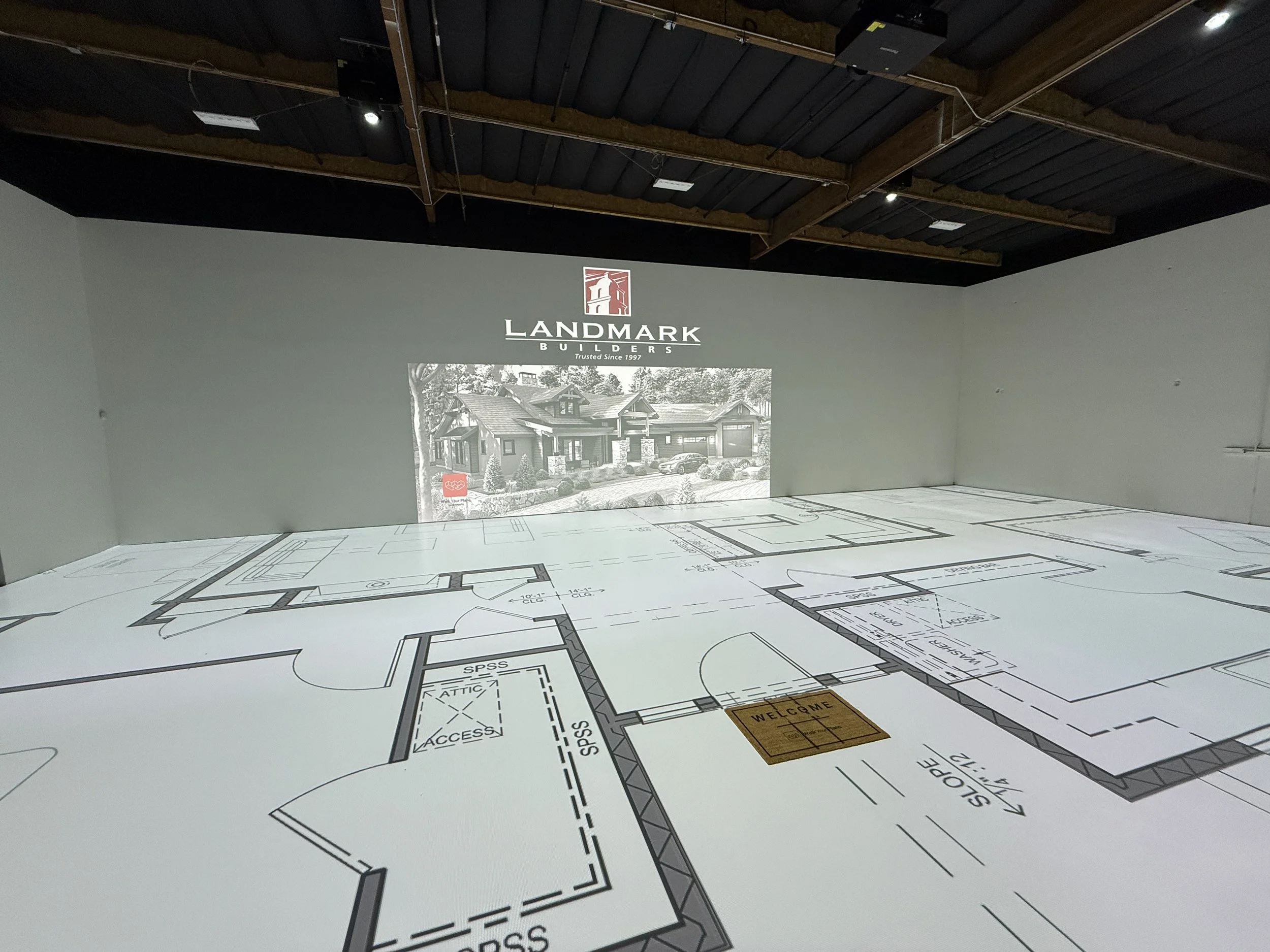 Construction blueprint or architectural floor plan for a house project, with a projection showing a real house photo and the Landmark Builders logo.