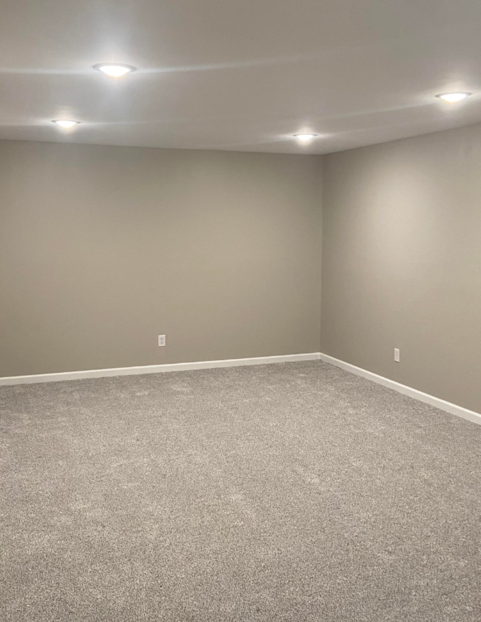 Empty room with beige carpet, plain gray walls, white baseboards, and ceiling lights.