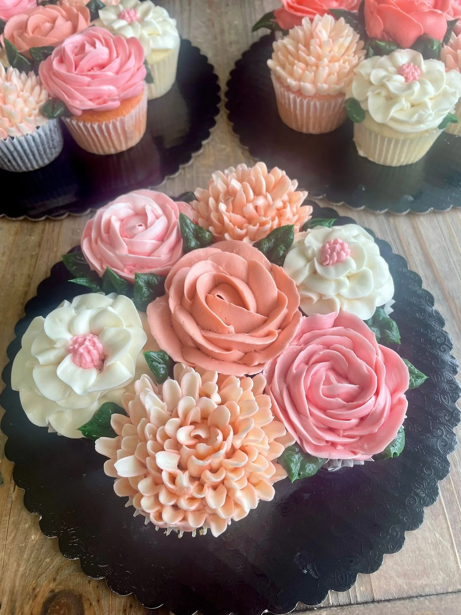 Decorative cupcakes with pink, white, and peach floral frosting designs arranged on a black platter.