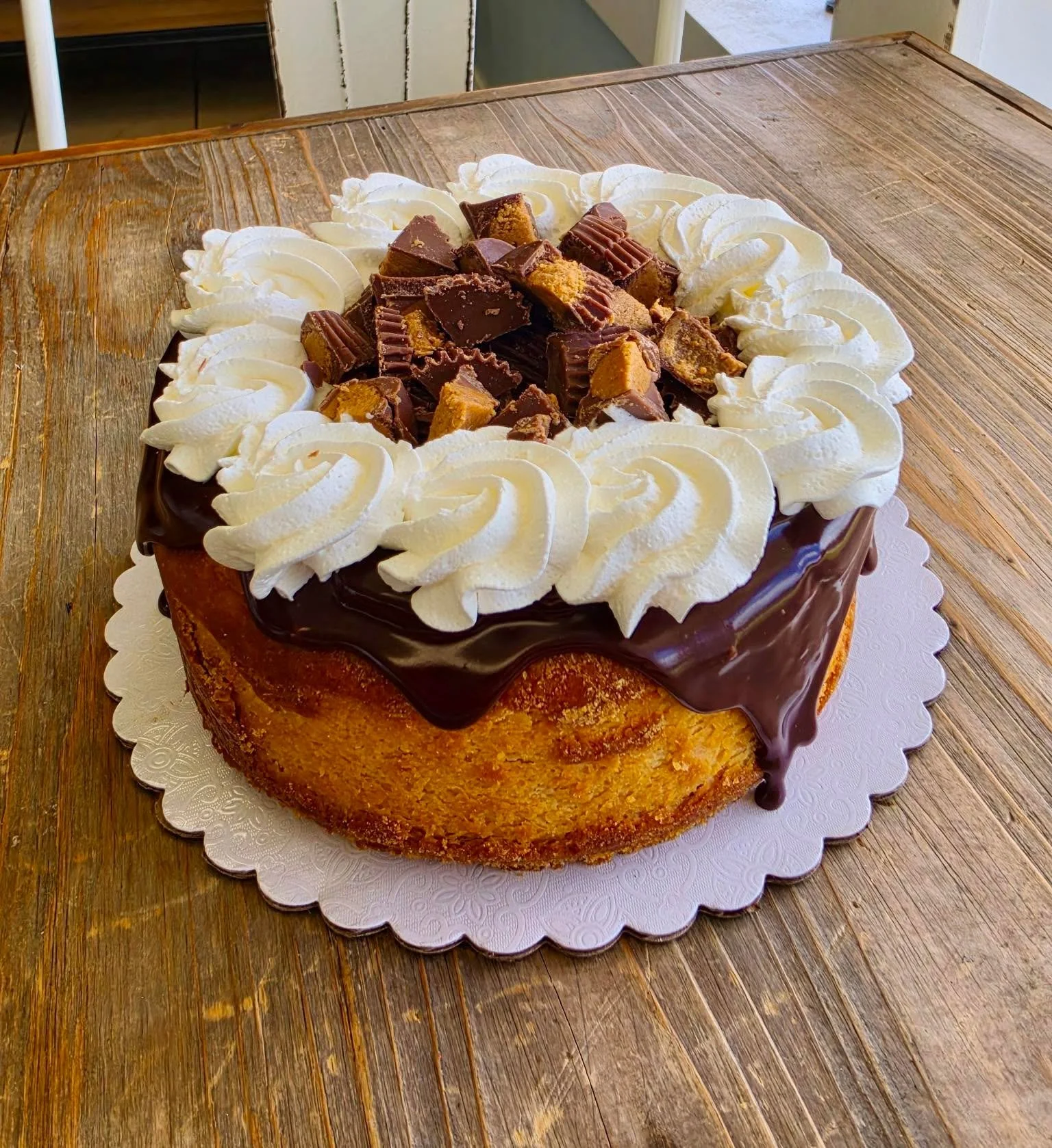 A round cake with chocolate frosting, topped with whipped cream and assorted chocolates, on a wooden table.