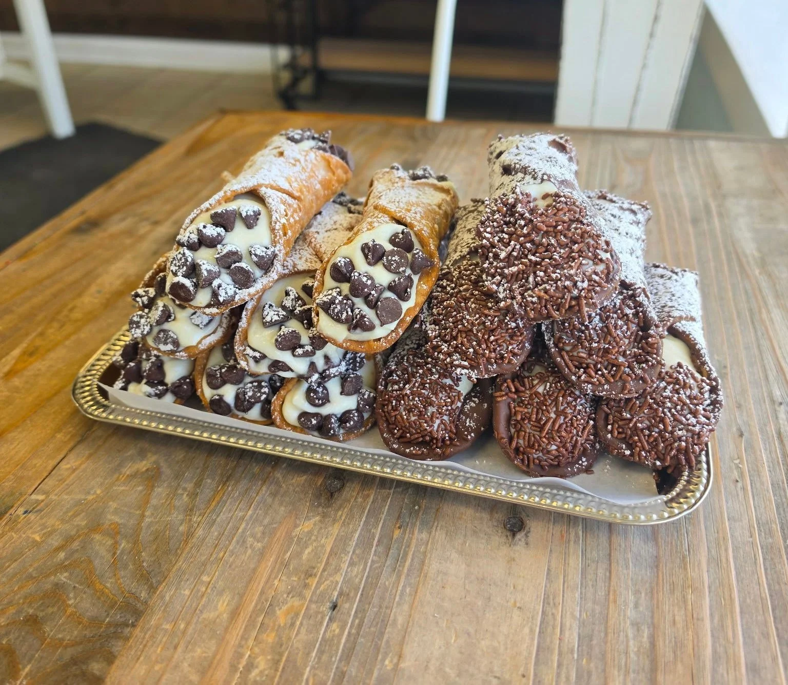 Tray of assorted cannoli with chocolate chips and sprinkles on a wooden table.