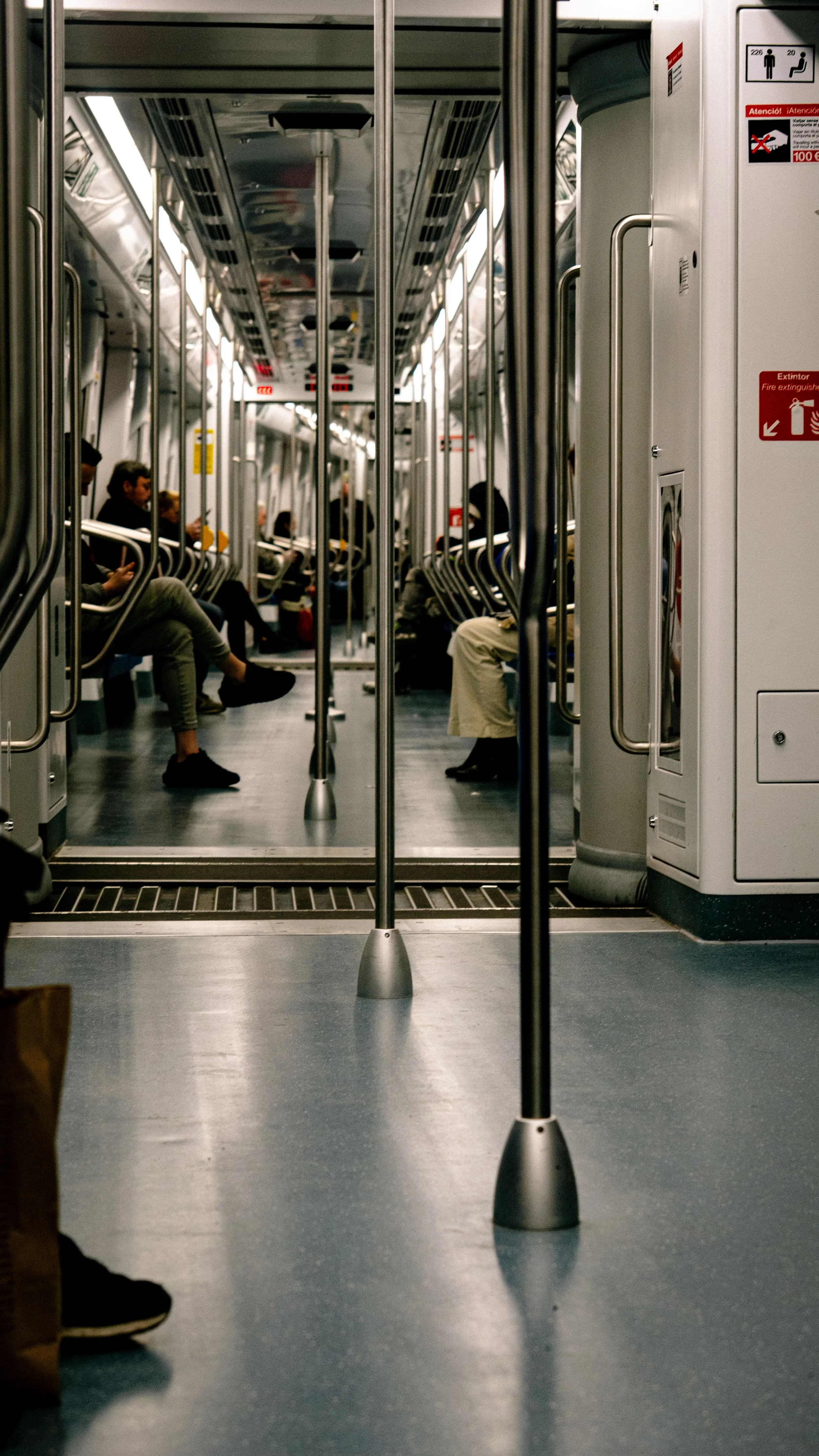 Inside a subway train with passengers seated and some using their phones, viewed through the door opening.