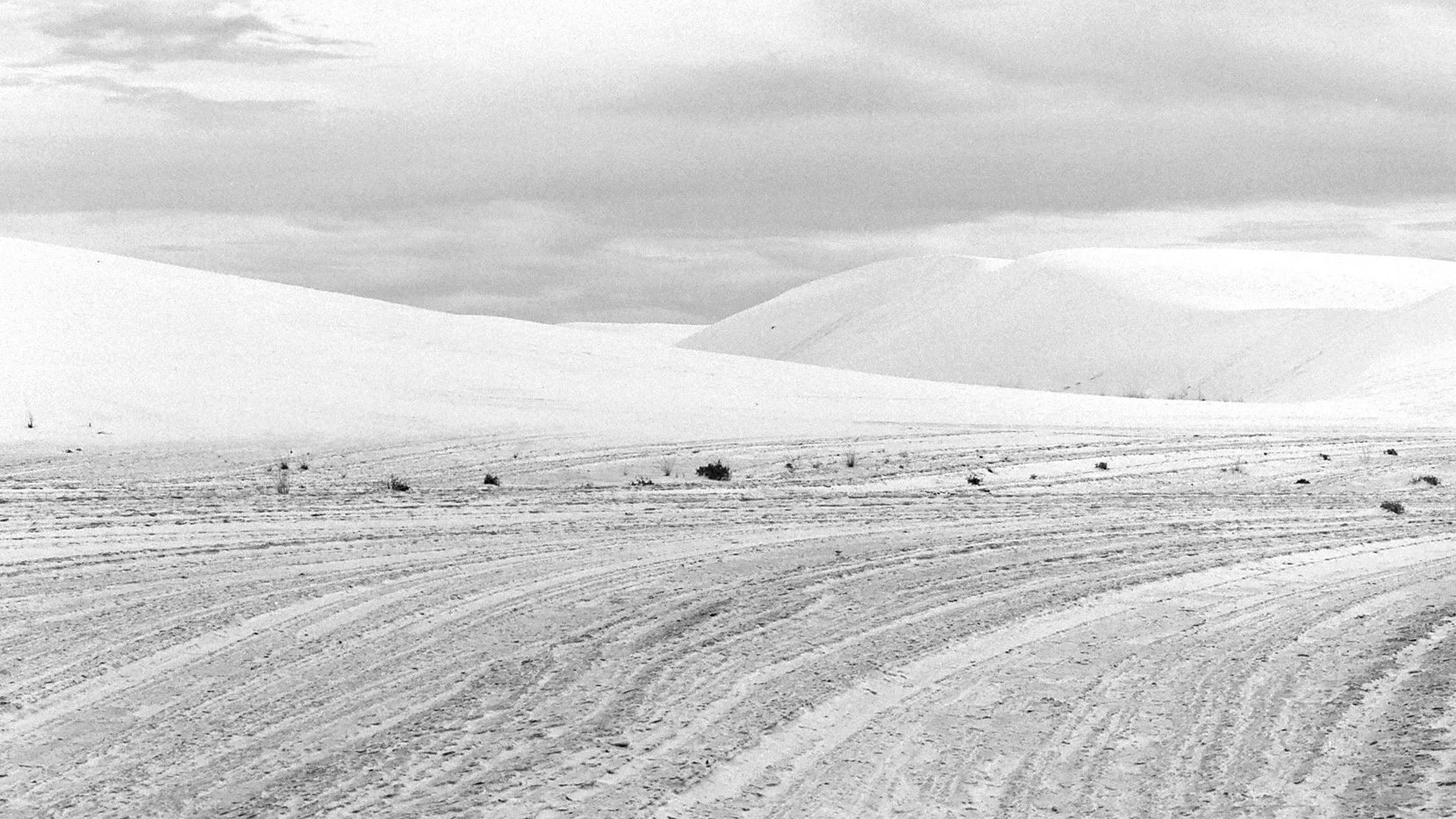Snow-covered landscape with rolling hills, a cloudy sky, and a dirt road in the foreground.