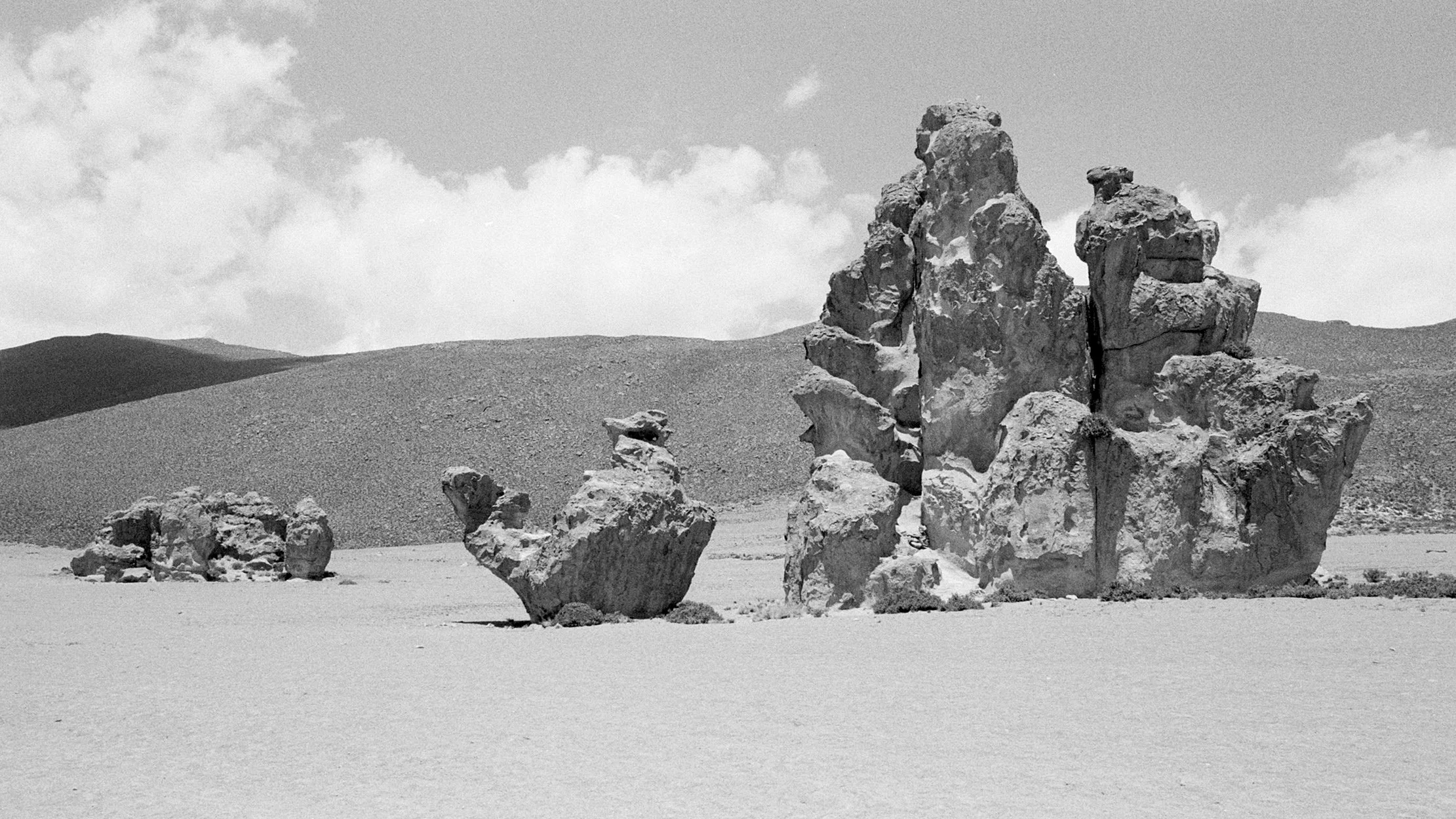 Black and white landscape of a desert with large rock formations and hills in the background.
