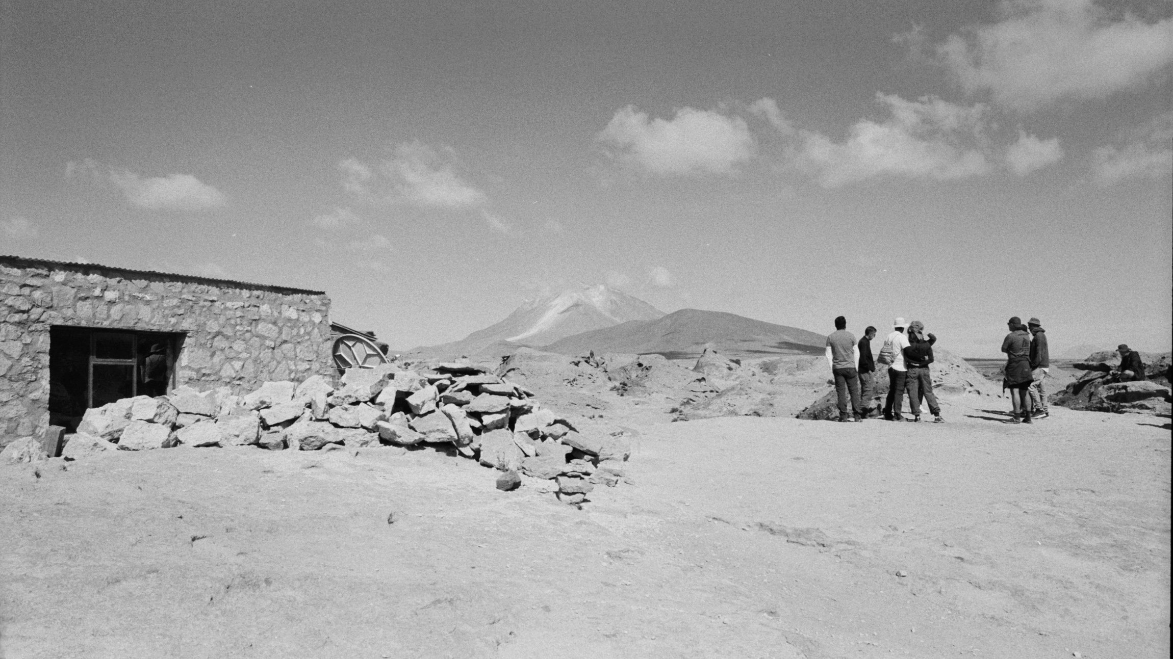 A group of people standing outdoors on rocky terrain with a mountain in the background.