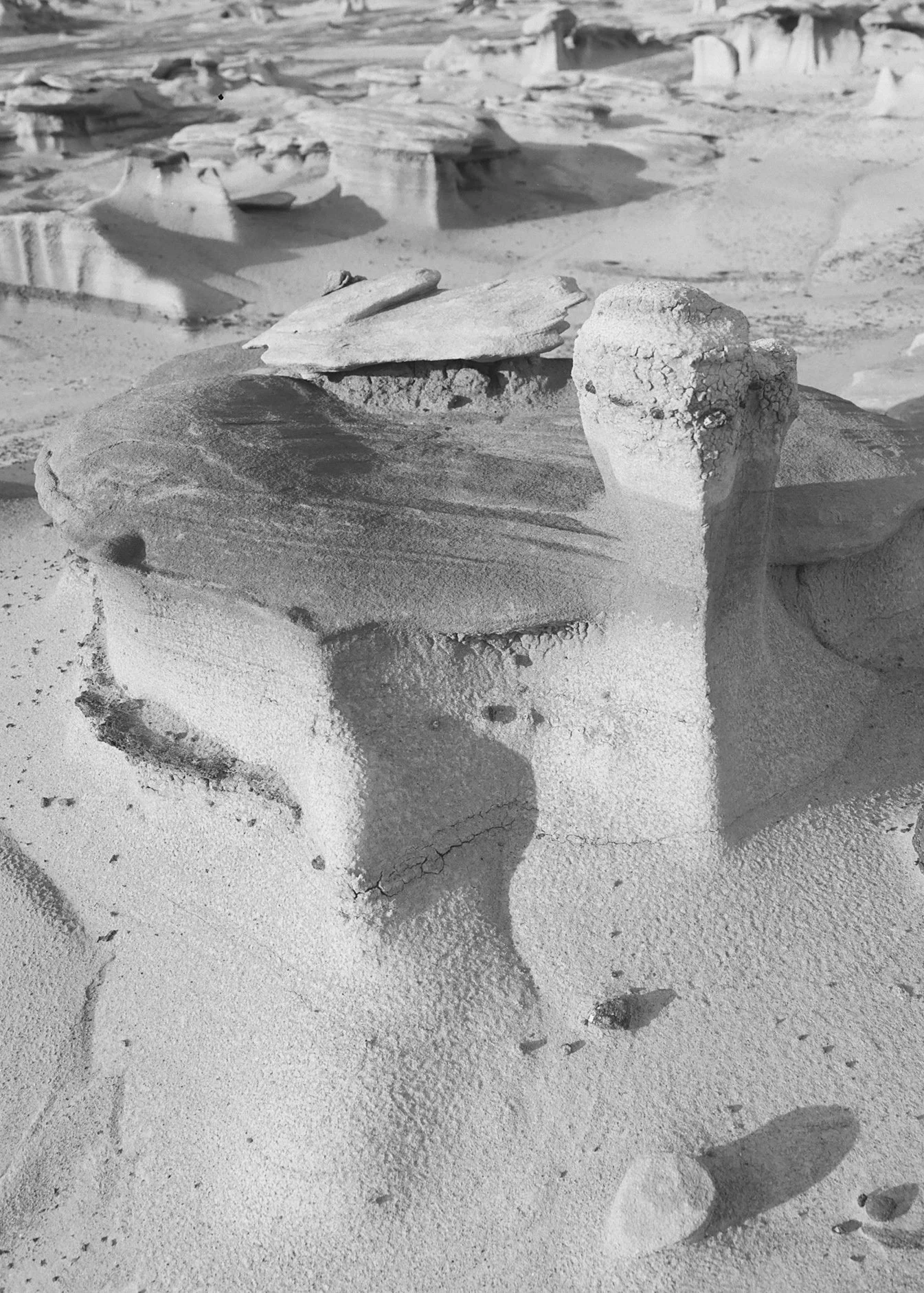 Close-up of a rock formation in a desert, with layered and cracked rocks and sand surrounding them.