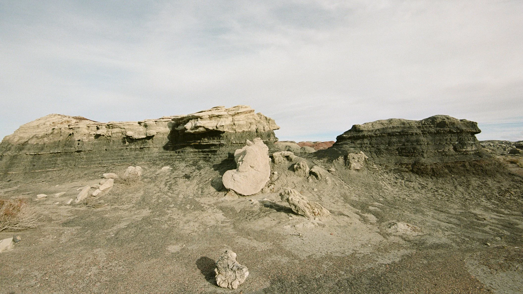 Desert landscape with layered rock formations and scattered boulders, under a partly cloudy sky.