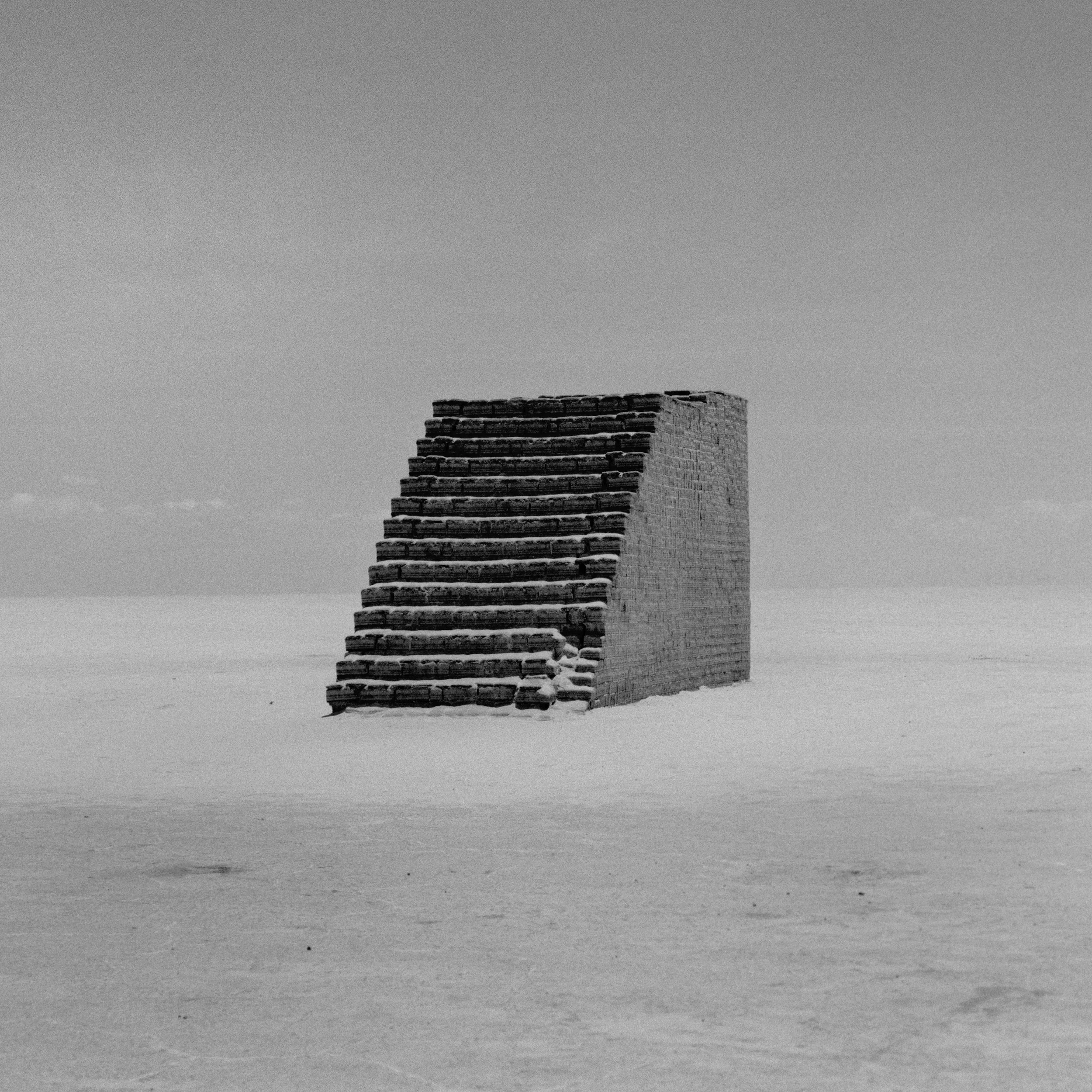 A set of stone stairs leading up to a brick wall in a barren, flat landscape with a cloudy sky.