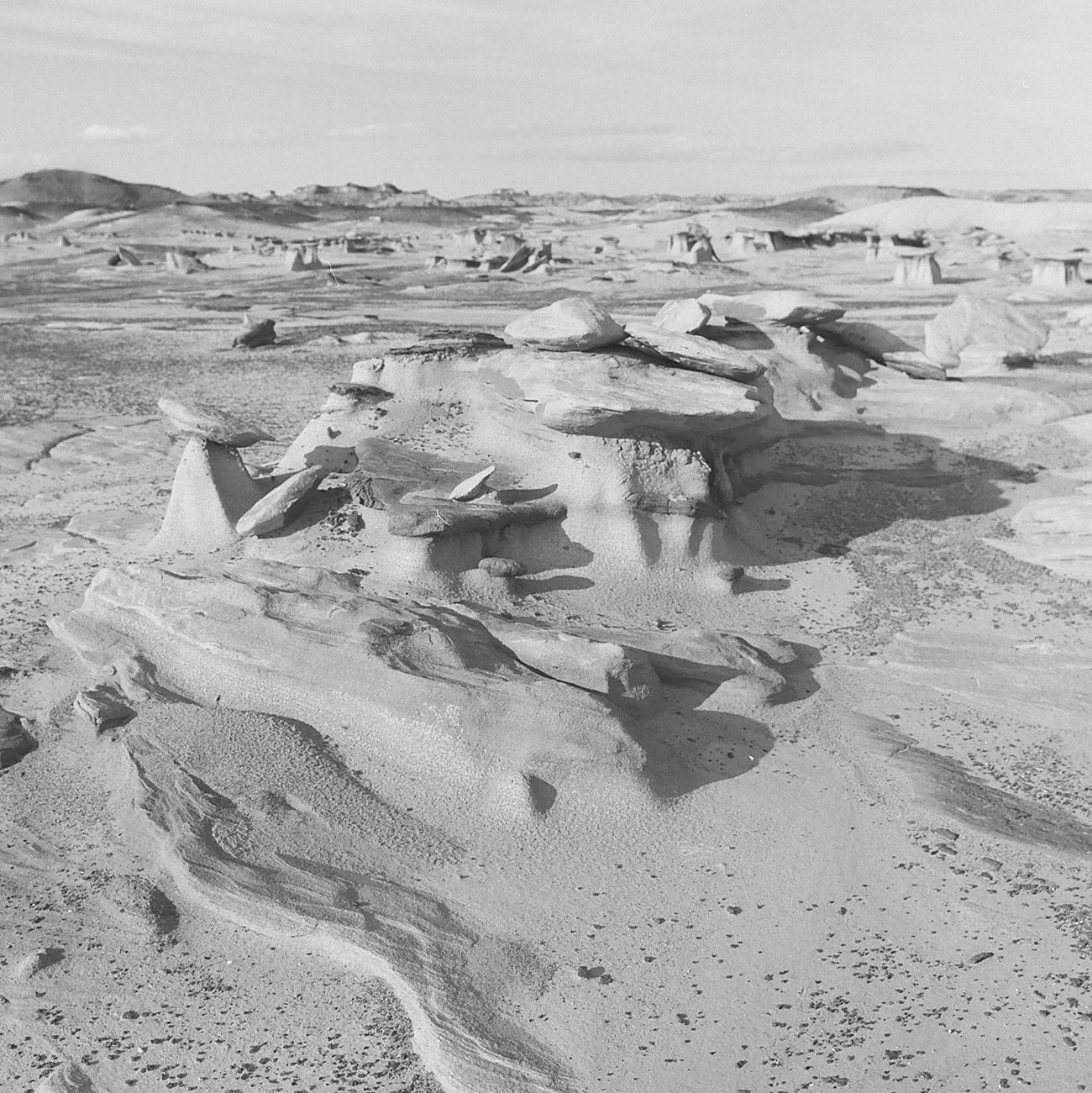 Black and white photo of a desert landscape with scattered rock formations and sand dunes in the background.