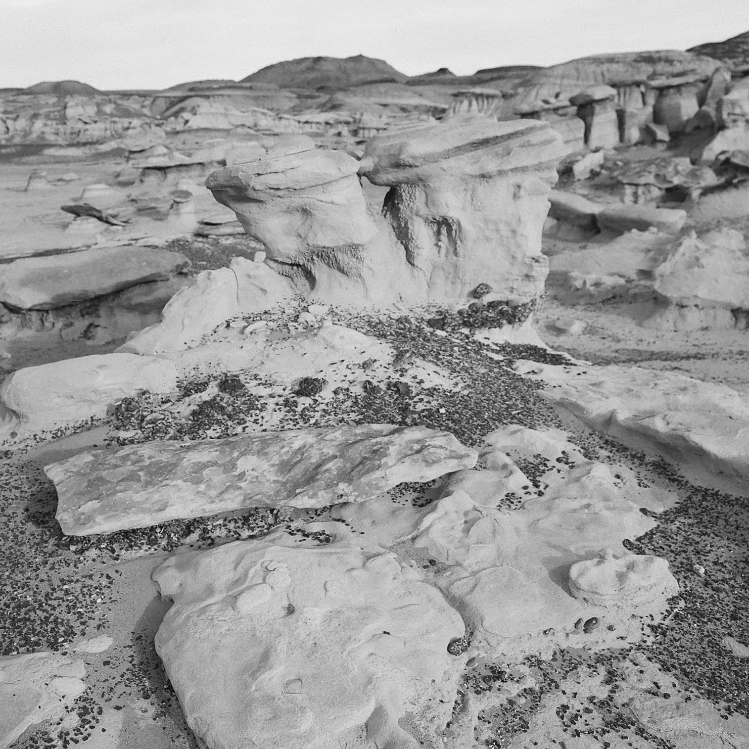 Black and white photo of eroded rock formations in a desert landscape with scattered small rocks and pebbles.