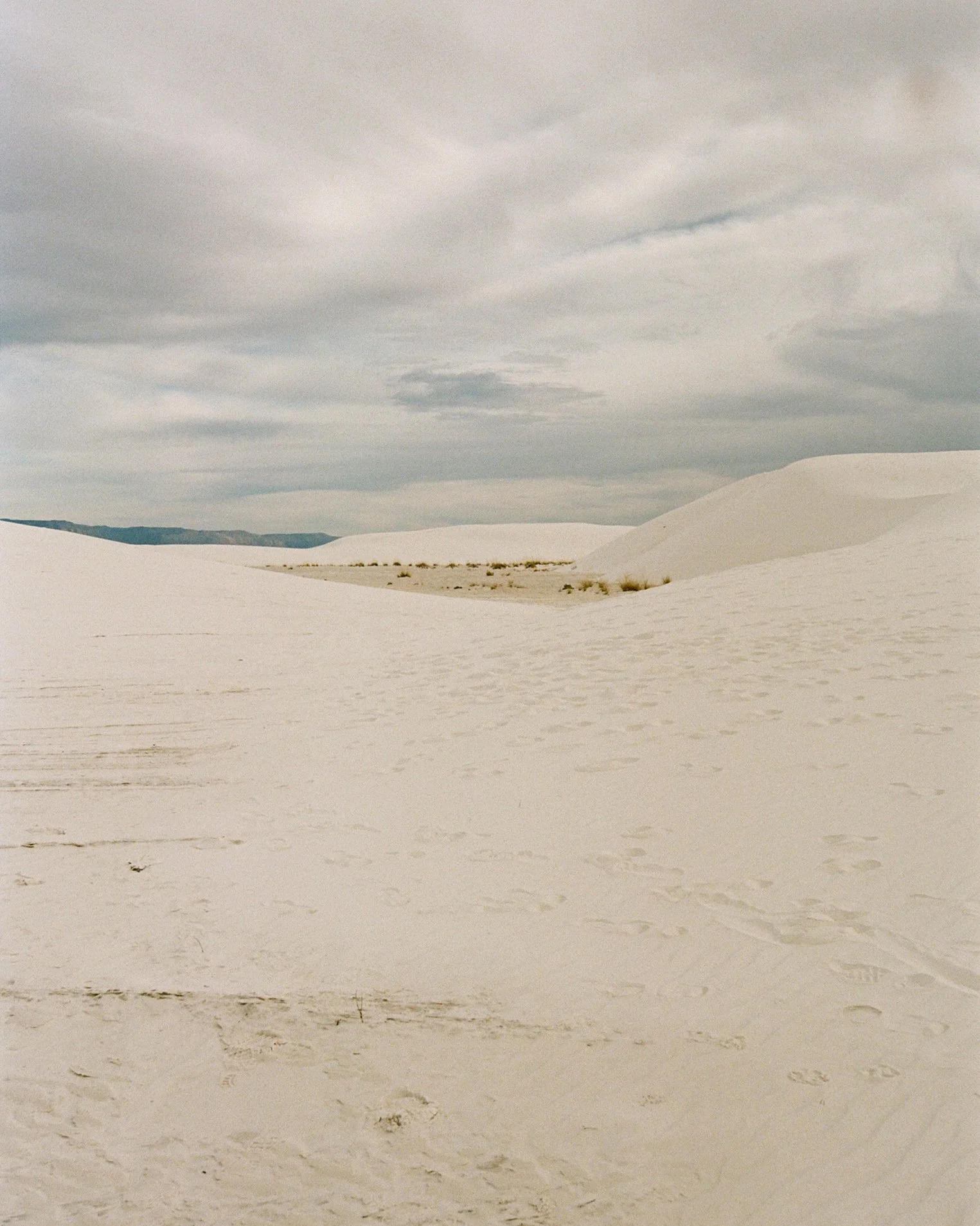 A landscape of white sand dunes under a cloudy sky.