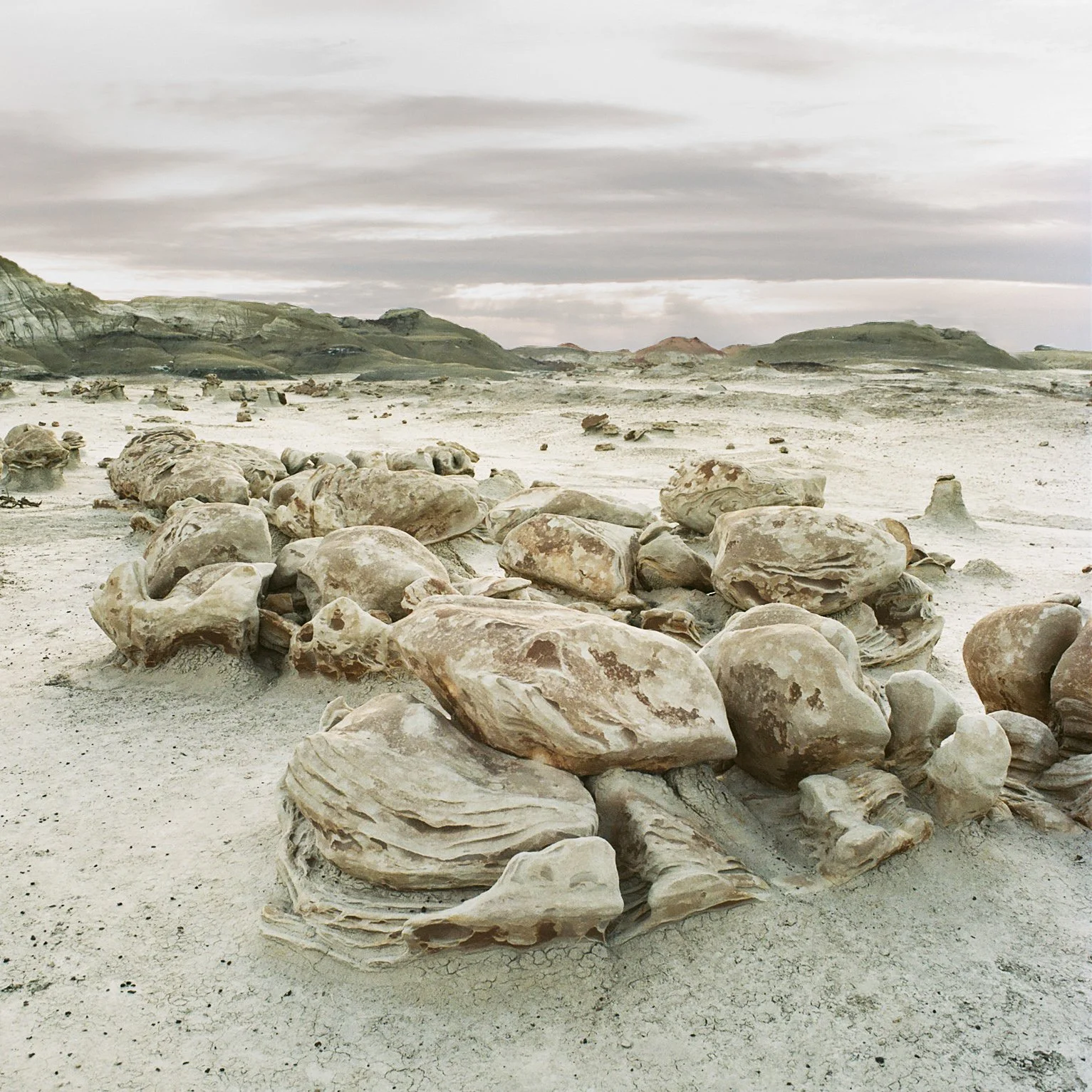 Stack of large, weathered rocks on a desolate, sandy landscape with rolling hills and a cloudy sky in the background.
