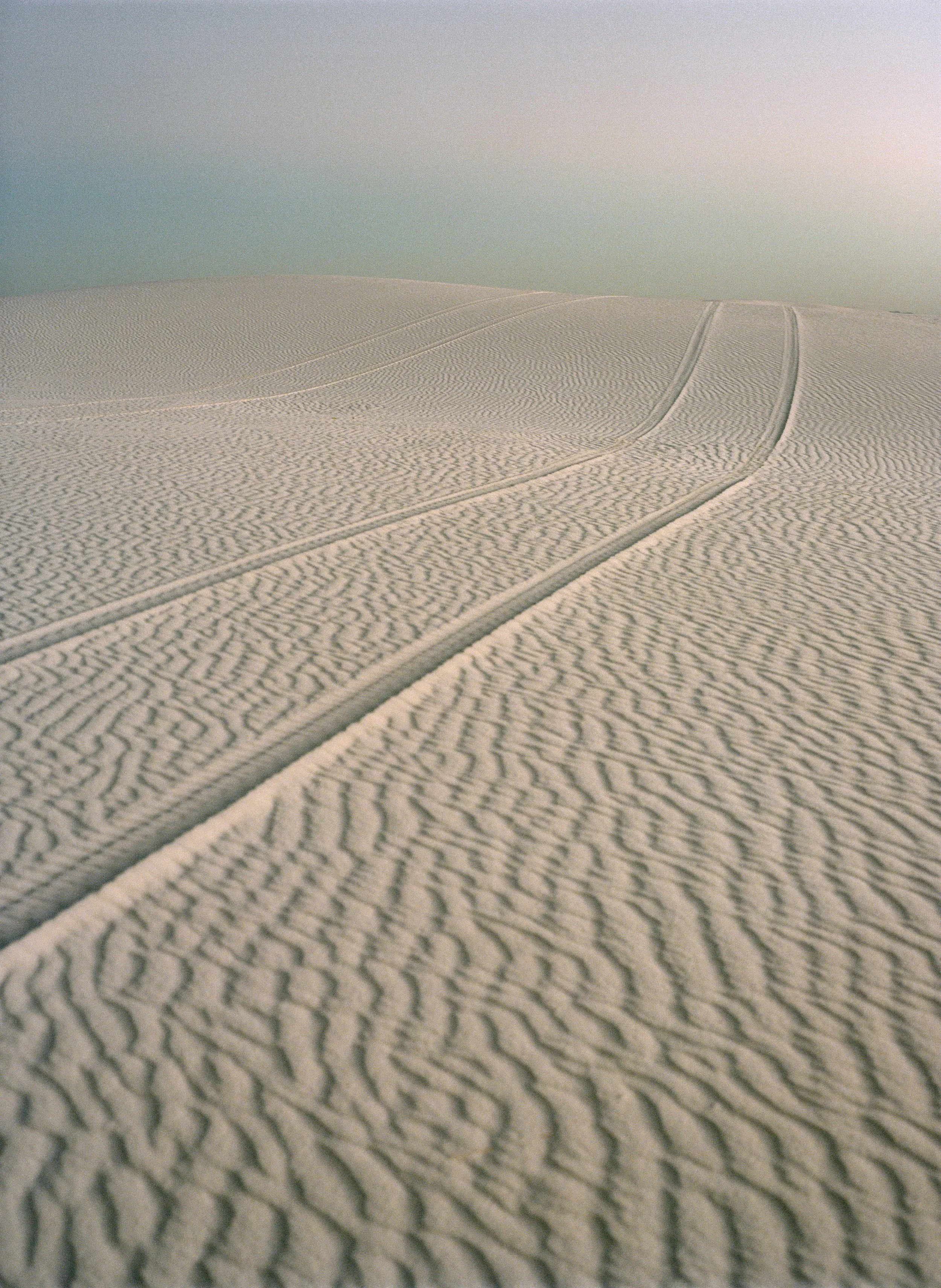 Sand dunes with tire tracks under a pastel sky