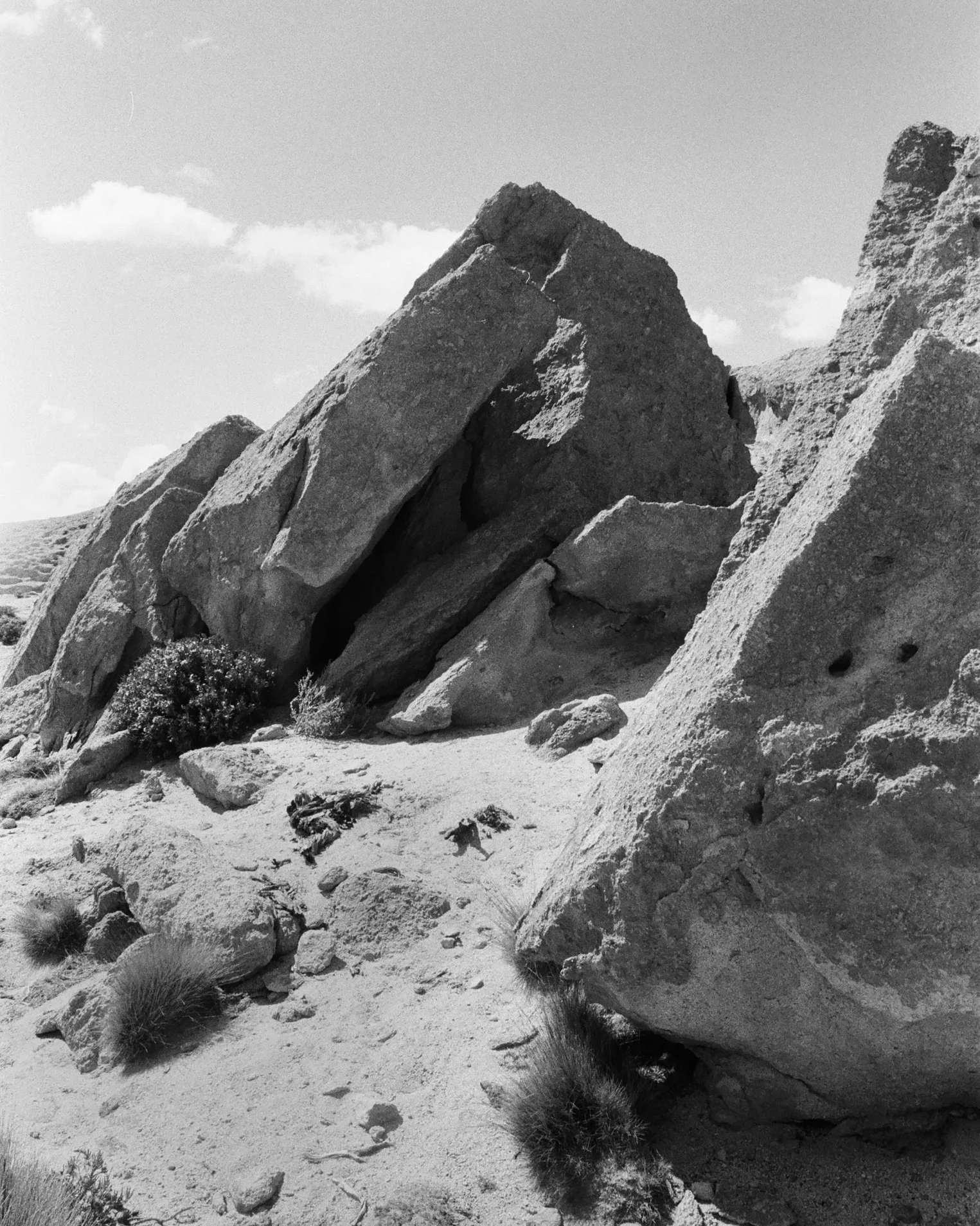 Black and white photograph of large, irregularly shaped rocks and boulders in a desert landscape with sparse vegetation and a partly cloudy sky.