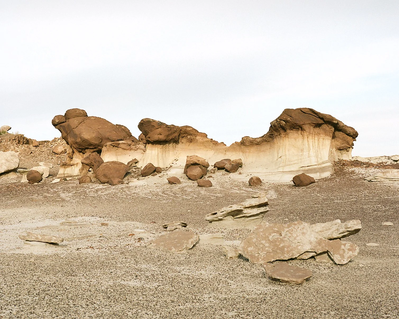 Desert landscape with large rock formations and scattered stones on sandy ground under a cloudy sky.