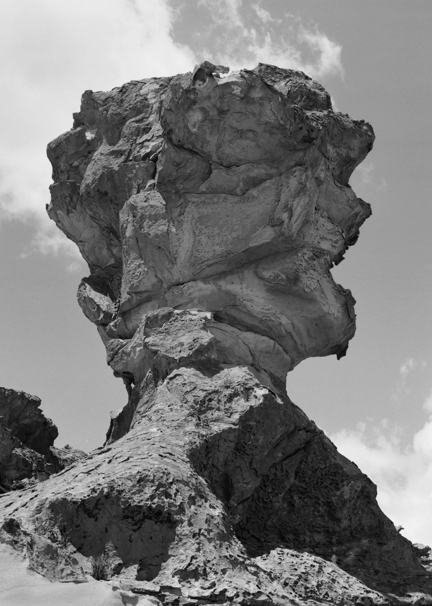 A large rock formation resembling a human head, with the profile facing left, set against a partly cloudy sky.