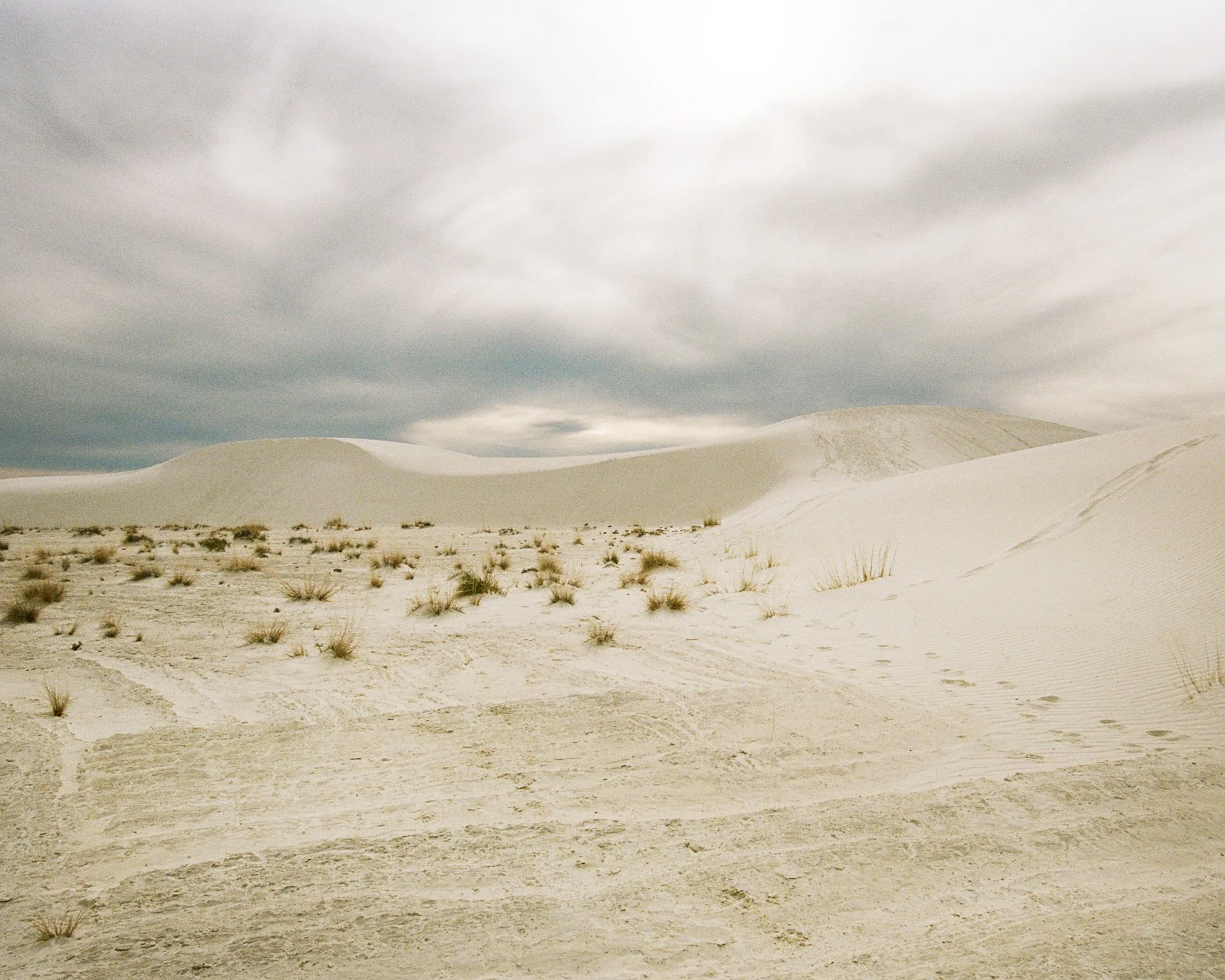 White sand dunes with sparse vegetation under a cloudy sky.