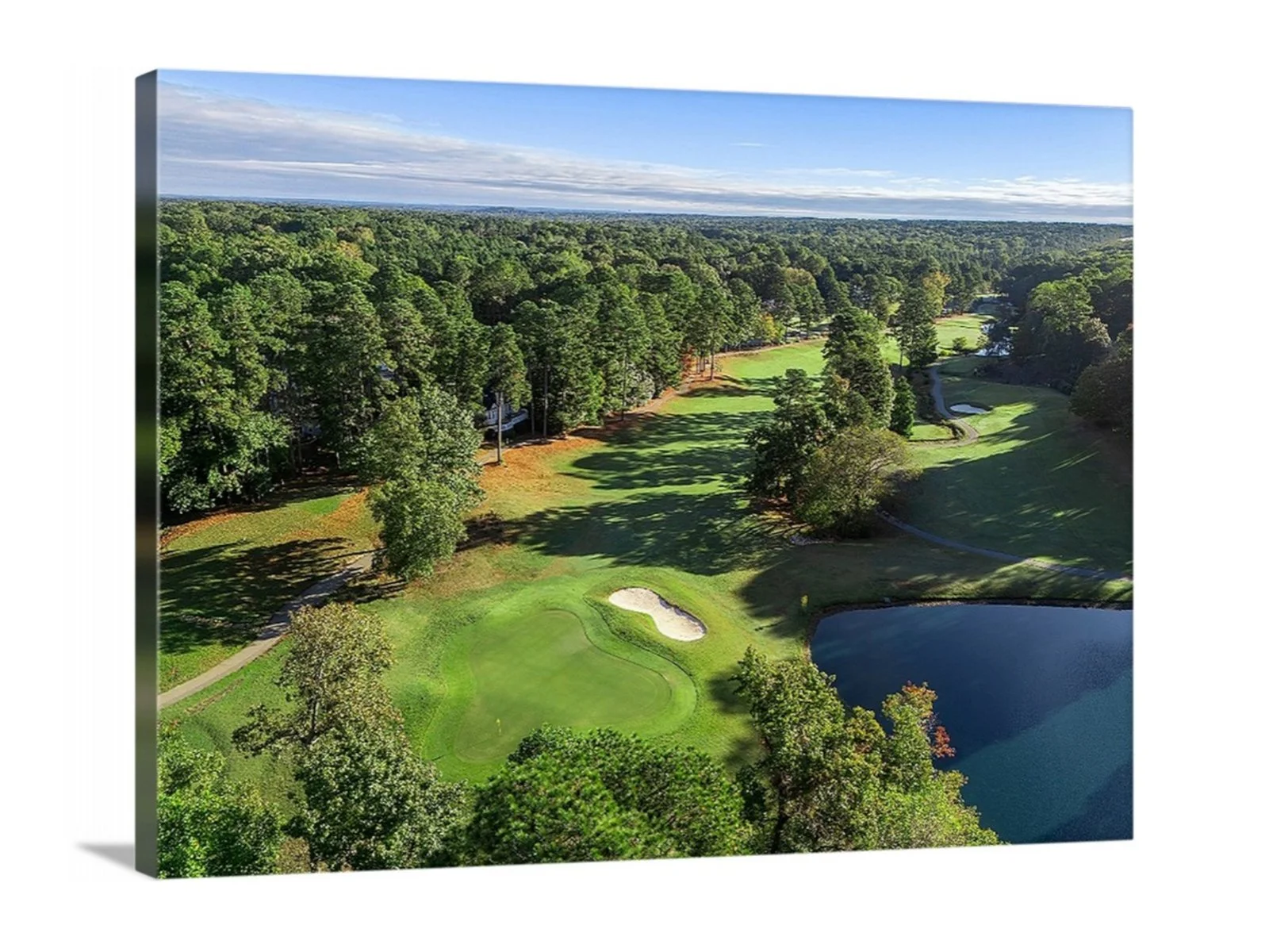 Aerial view of a golf course with green fairways, sand traps, water hazards, surrounded by trees under a partly cloudy sky.