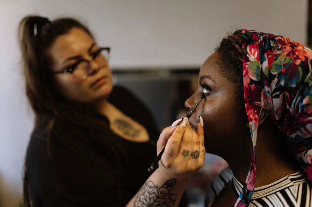A makeup artist applying eyeshadow to a woman with a floral headscarf.