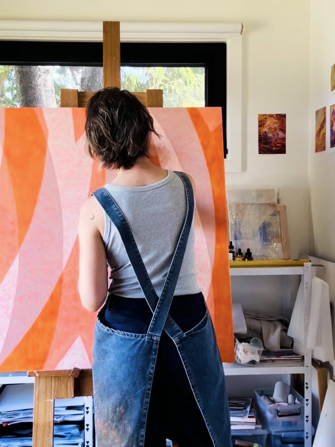 Artist in blue apron painting large geometric orange painting on easel