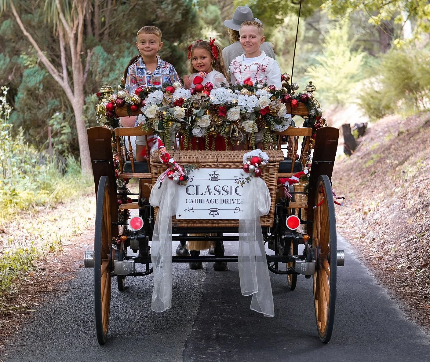 A decorated horse-drawn carriage with three children sitting inside, adorned with flowers, celebrating a classic carriage drive.