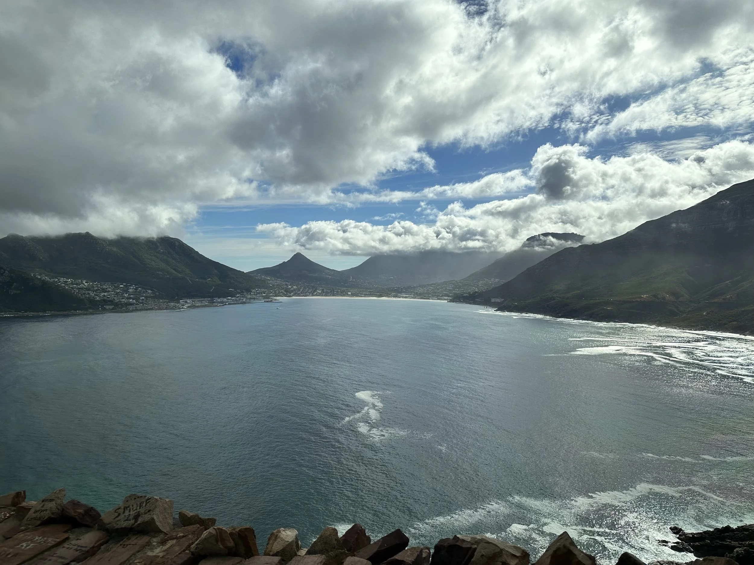 A panoramic view of a large body of water surrounded by green mountains under a sky with scattered clouds.