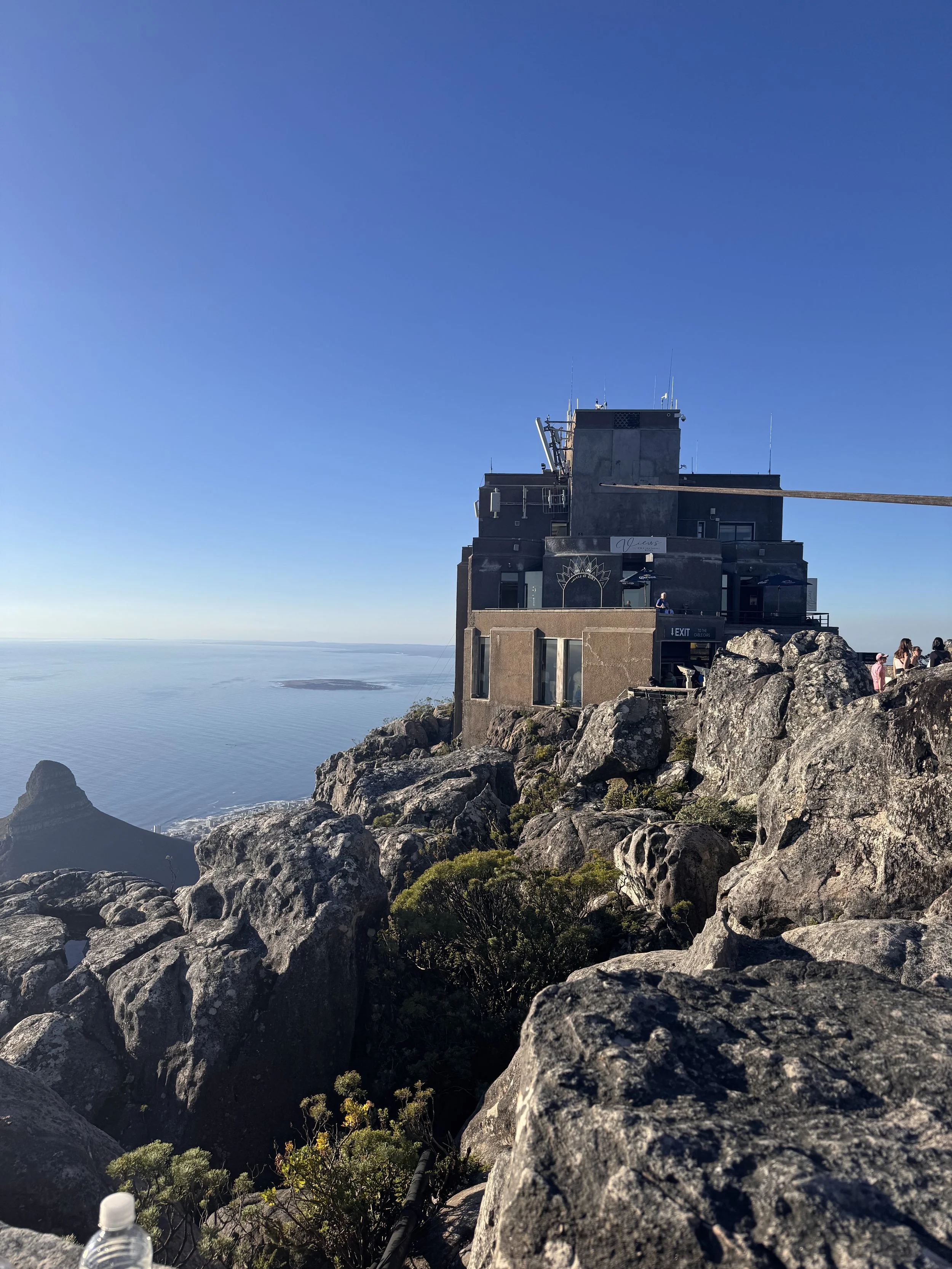 A building on a rocky hillside overlooking the ocean with a clear blue sky.