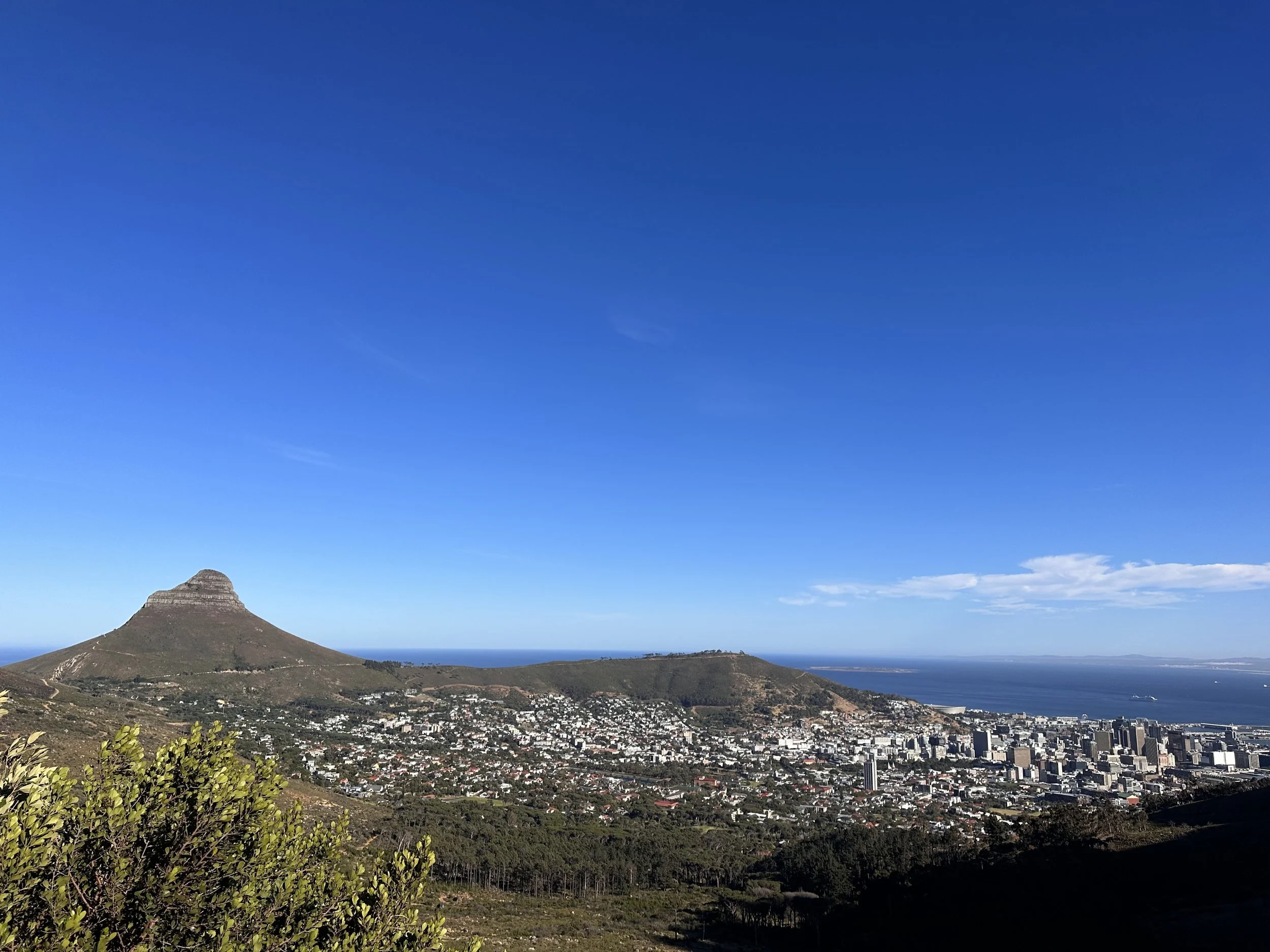 A landscape view of Cape Town, South Africa, featuring Table Mountain, urban area, and ocean under a clear blue sky.