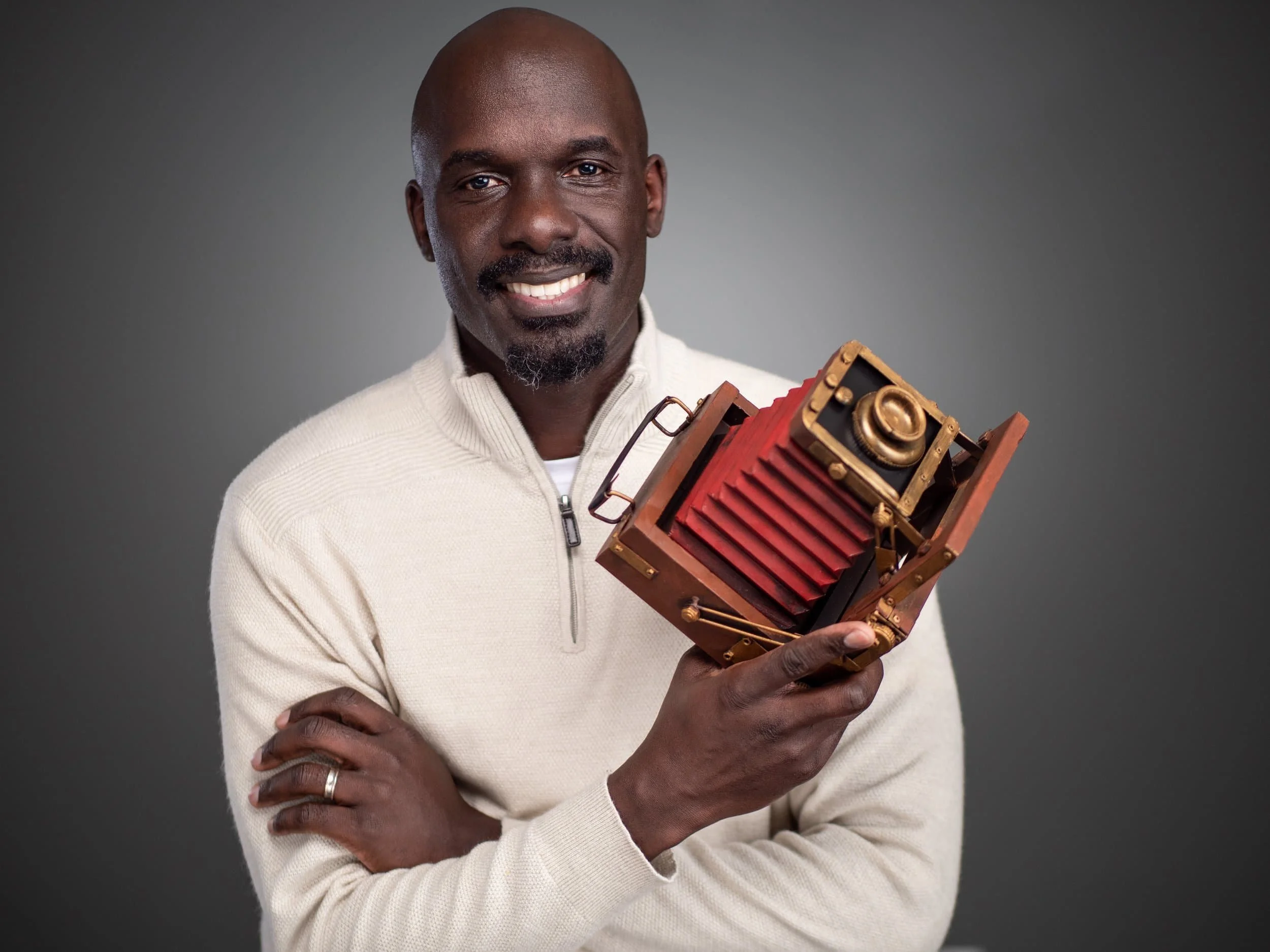 Nathan Ochole Principal Photographer at HeadshotPix smiles and holds a vintage camera in his hand