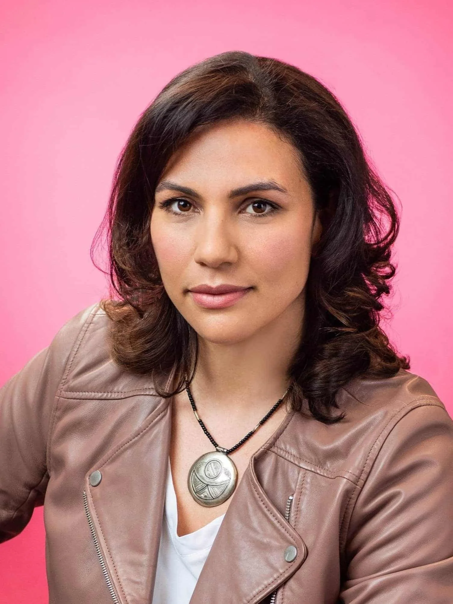young woman looking at the camera during a photoshoot against a  pink background