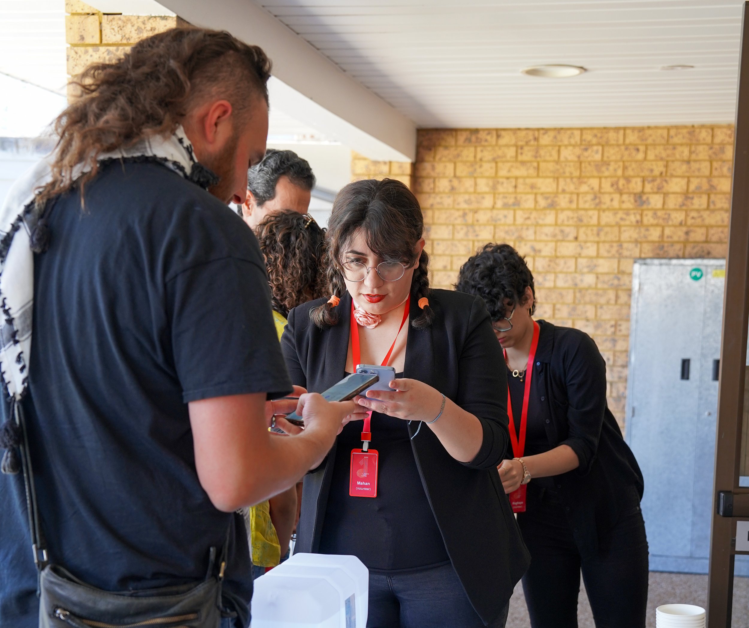 People using smartphones at an event, wearing badges.
