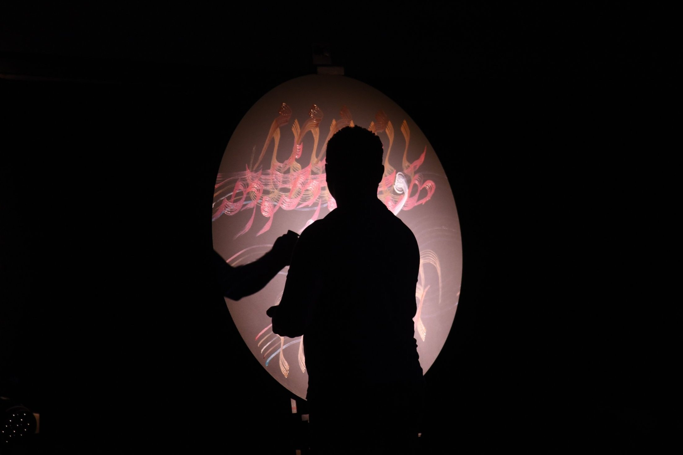 Silhouette of a person in front of a circular illuminated surface with colorful abstract patterns.