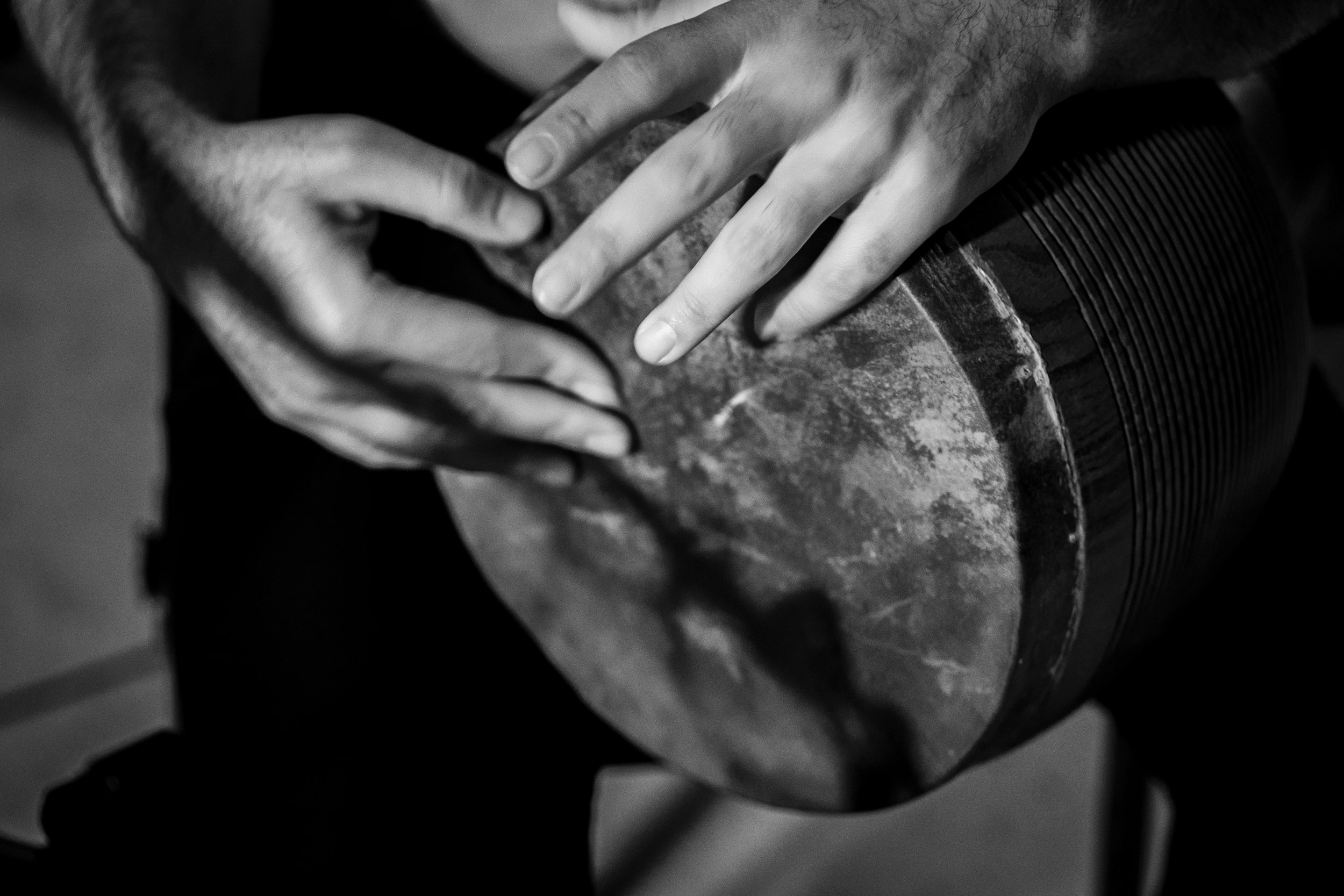 Close-up of hands playing a darbuka drum, black and white.