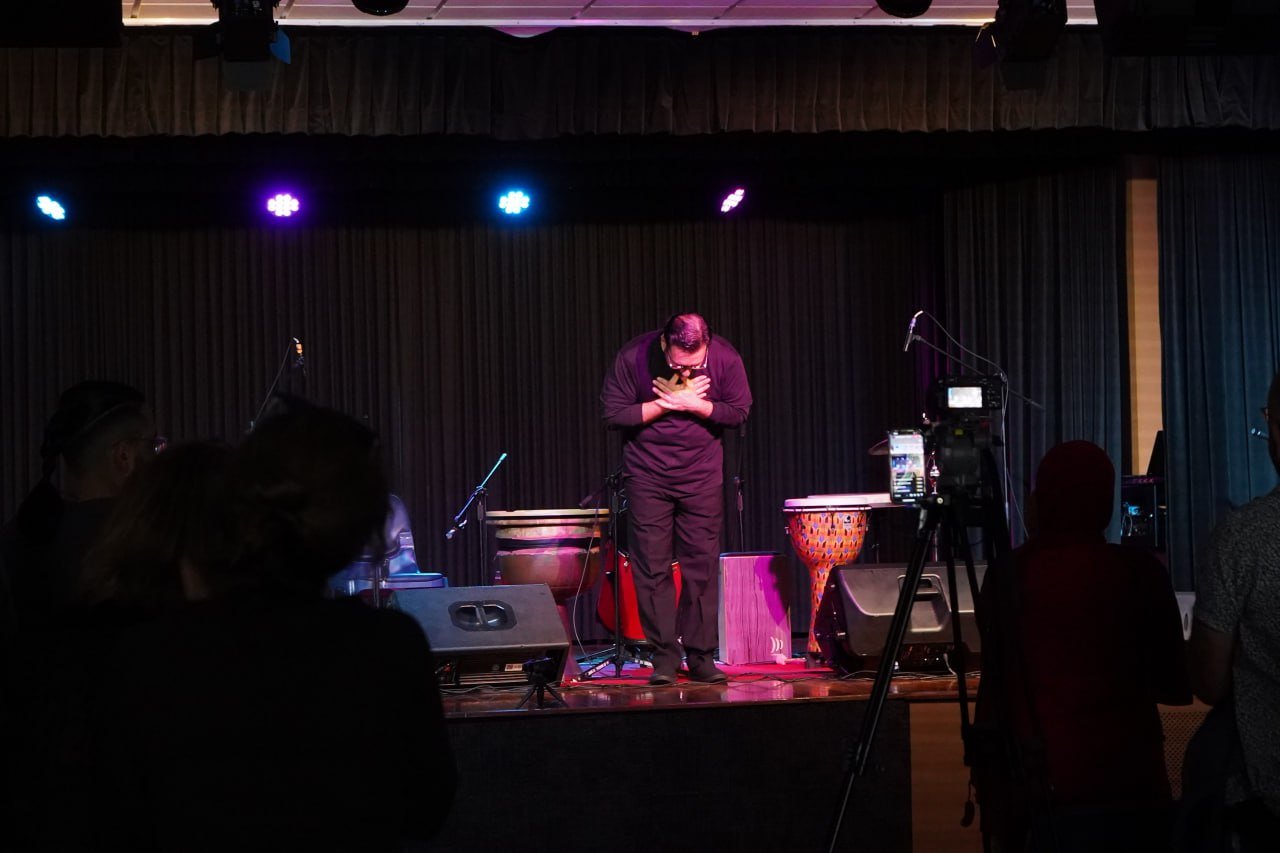 Performer bowing on stage with instruments and audience in foreground.