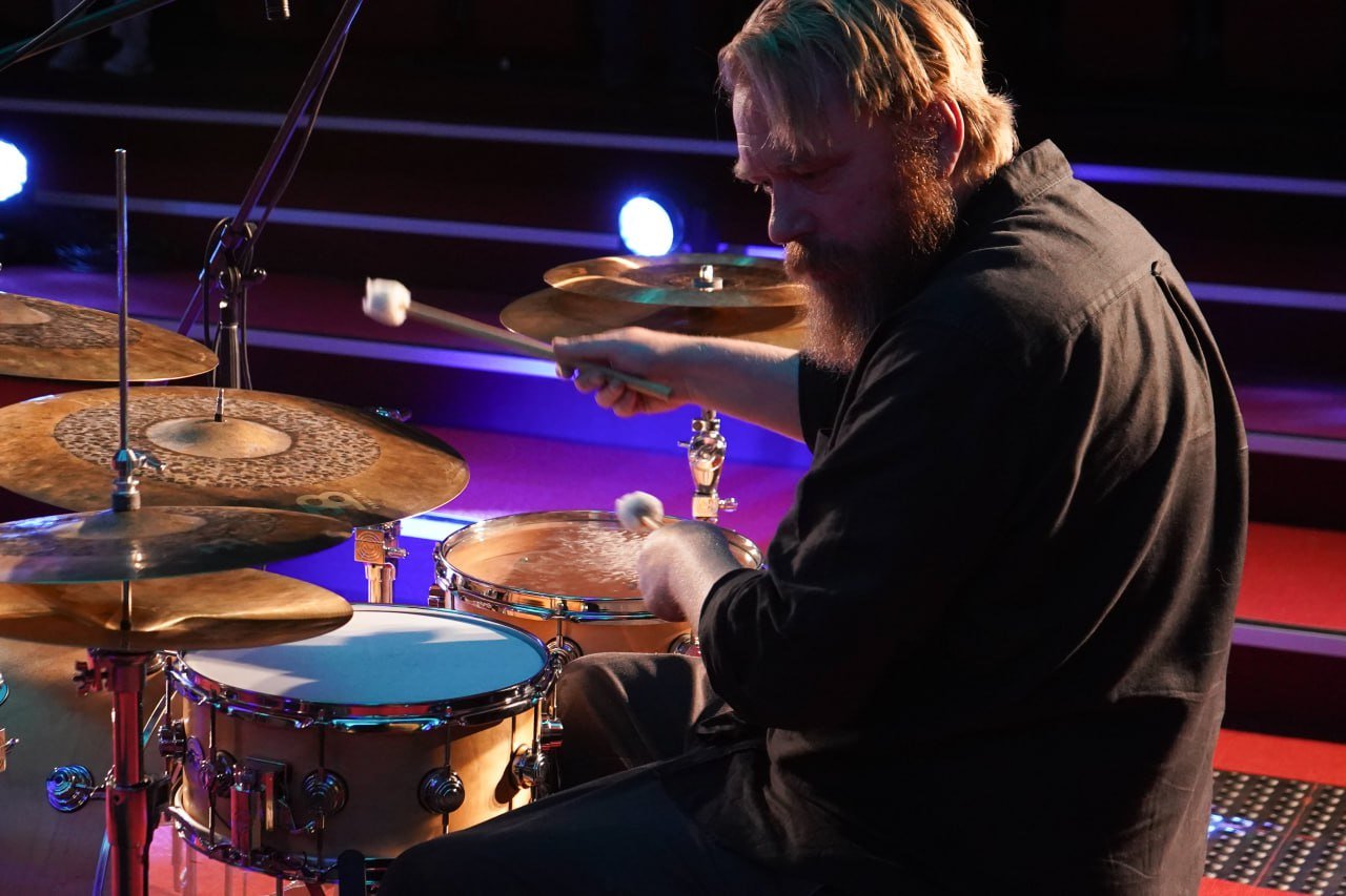 Man playing drums with brushes on a drum set under stage lighting
