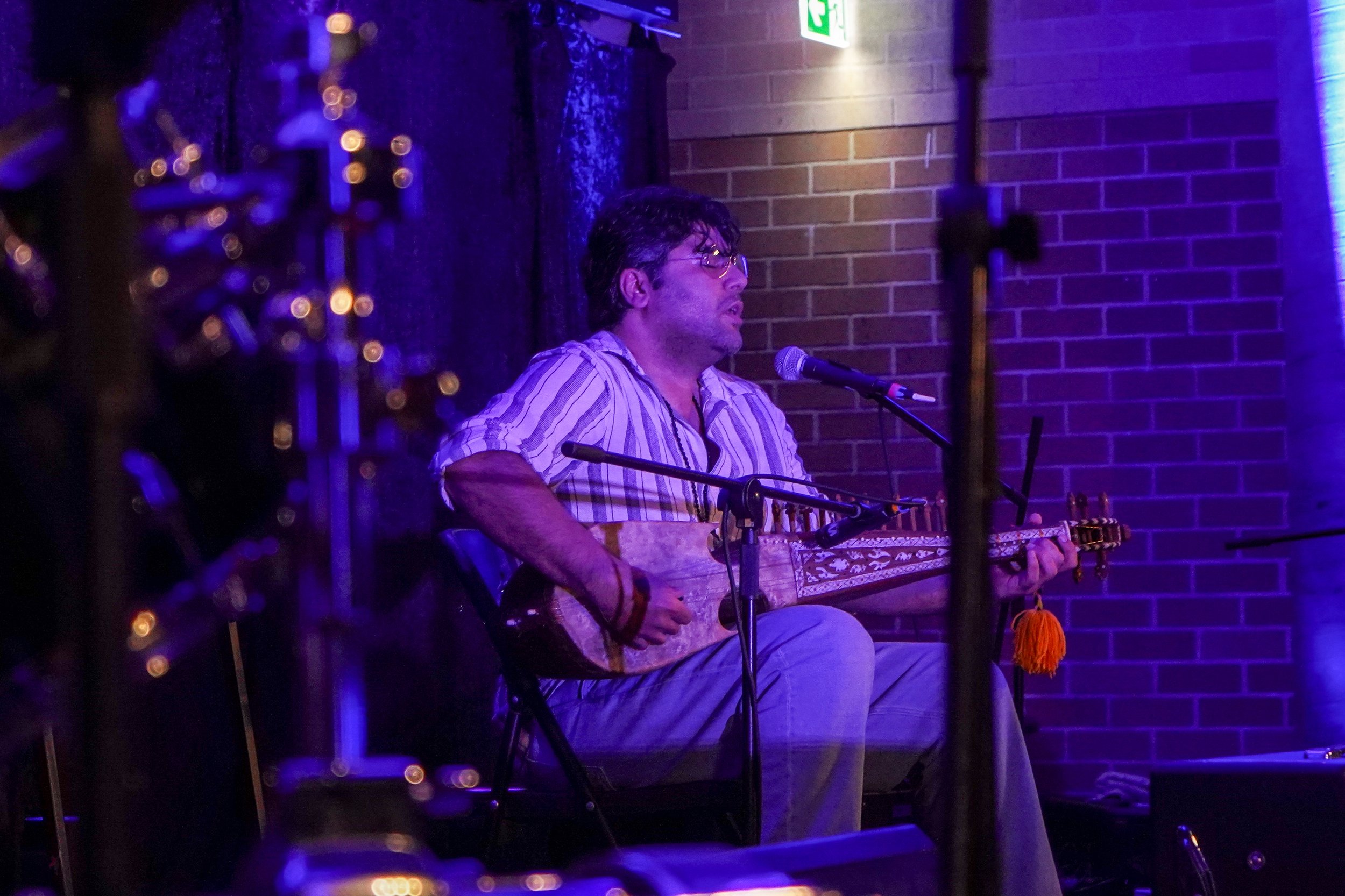 Person playing a stringed instrument on stage with a microphone, under purple lighting.