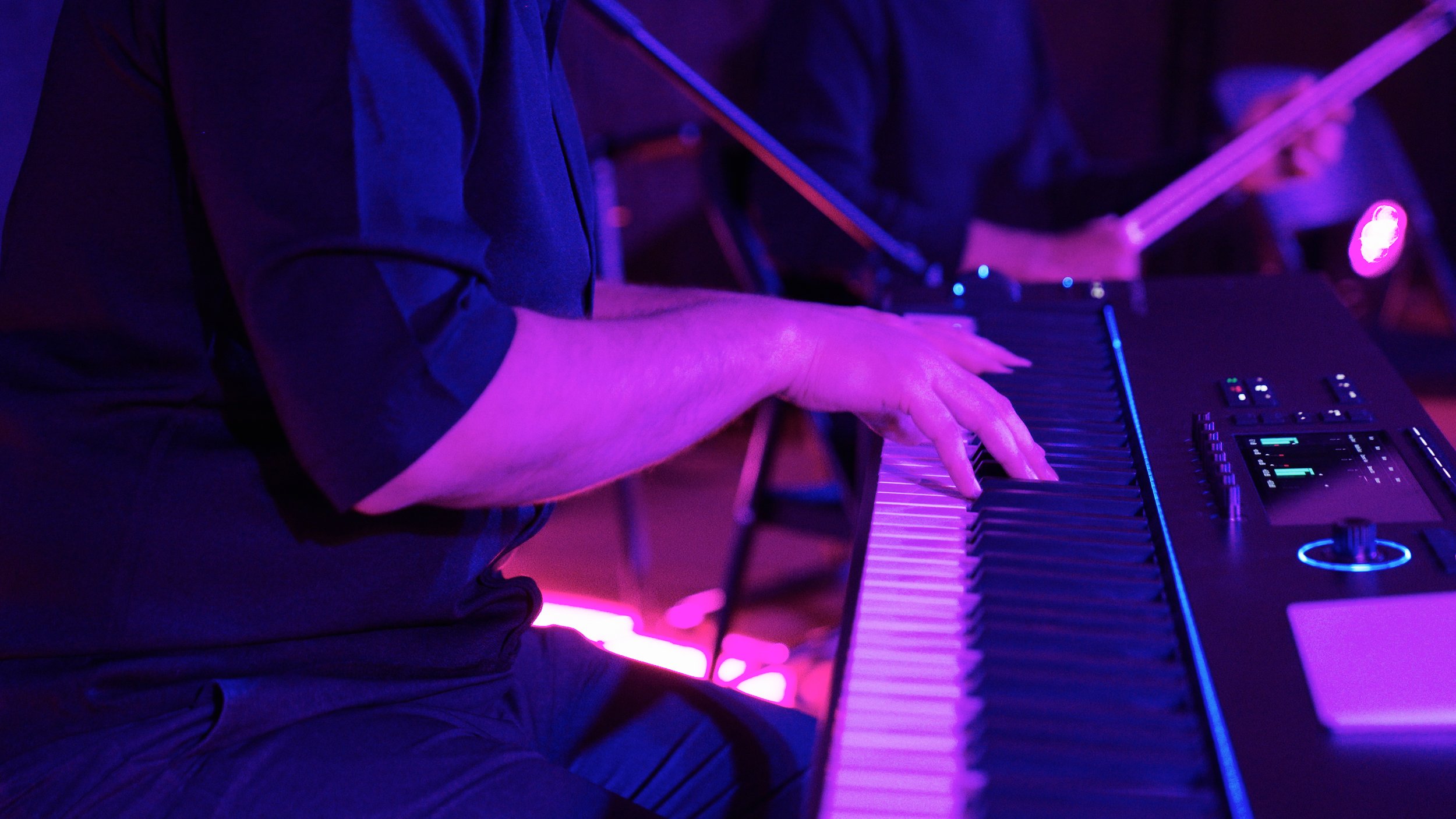 Person playing an electric keyboard with purple stage lighting.