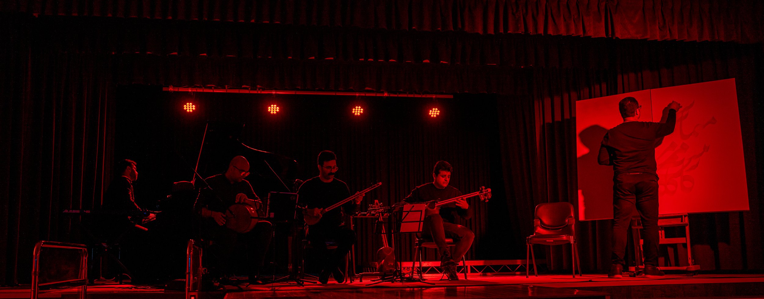 Musical performance on stage with live painting, red lighting, musicians playing string instruments, and an artist working on a large canvas.