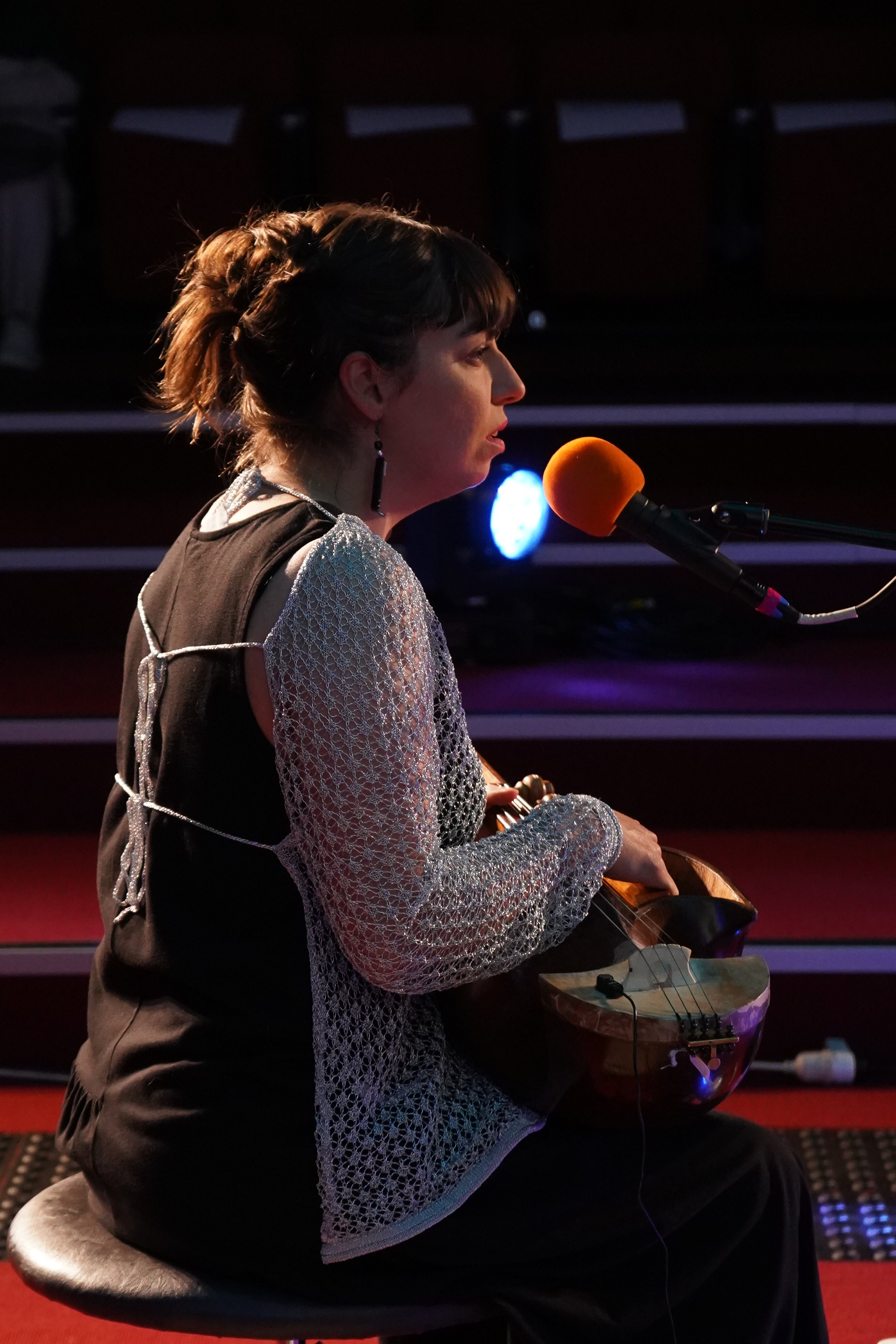 A woman playing a string instrument on stage with a microphone.
