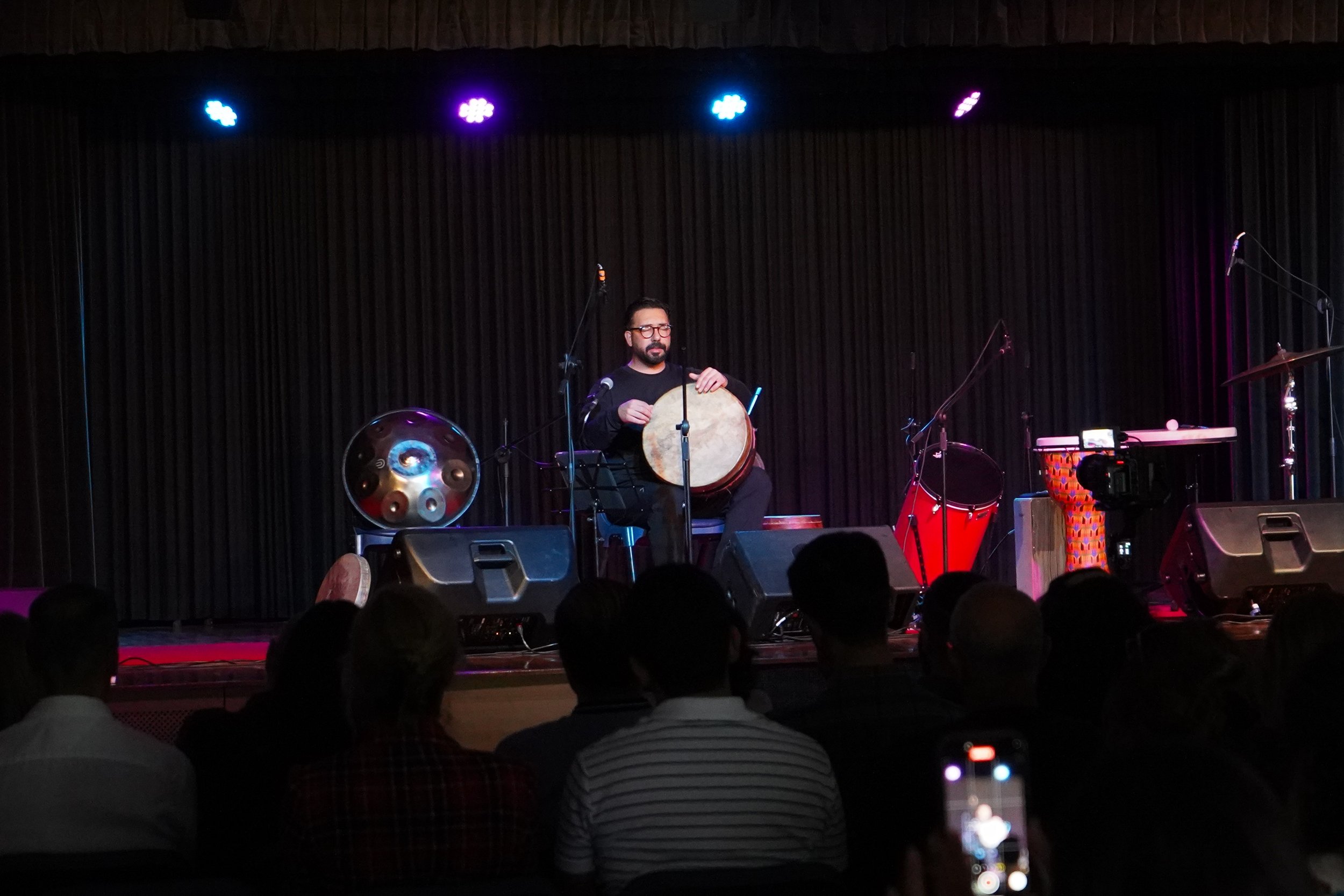 Musician playing drum on stage with audience watching