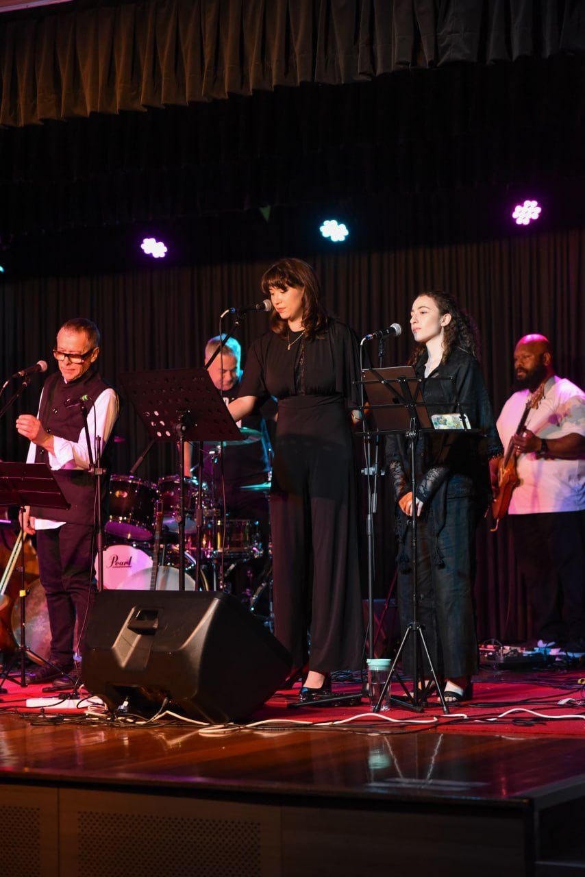 Live band performing on stage with musicians and vocalists under stage lights.